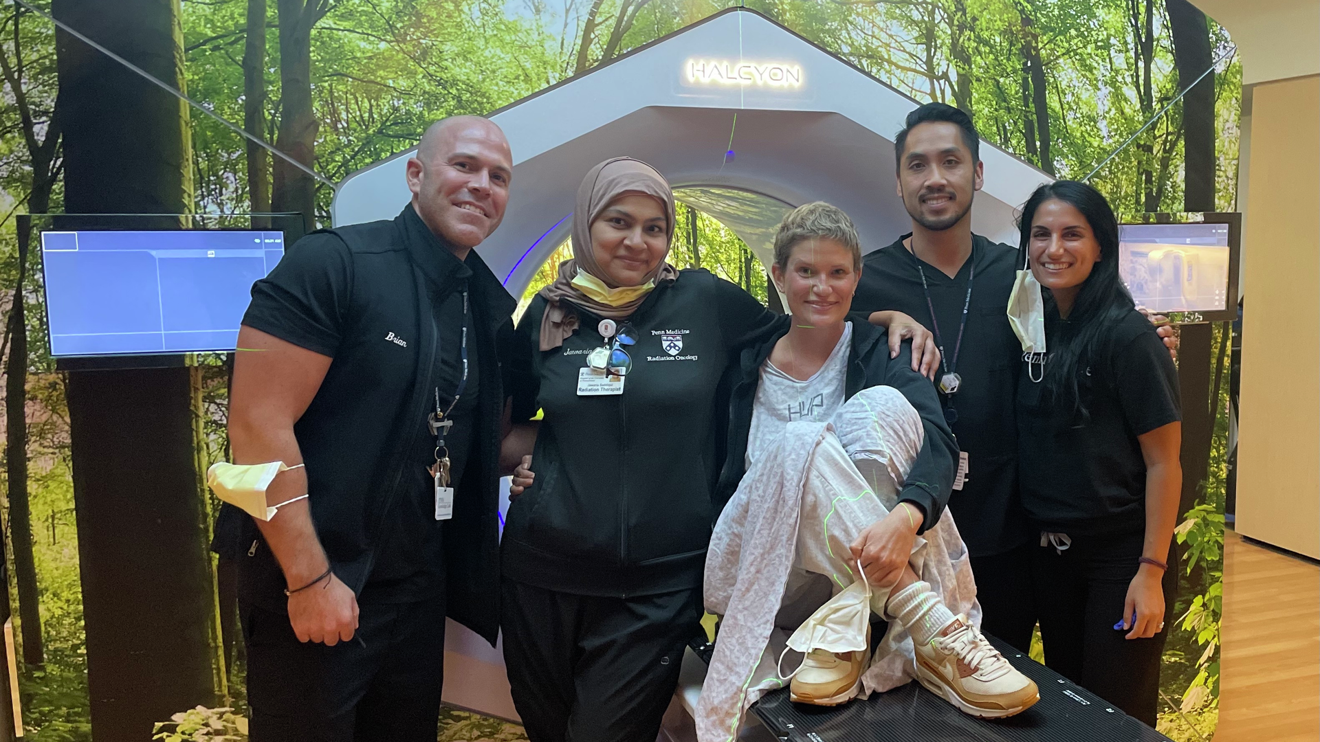 Kate Korson sits on a treatment bay for radiation, surrounded by her radiation oncology care team