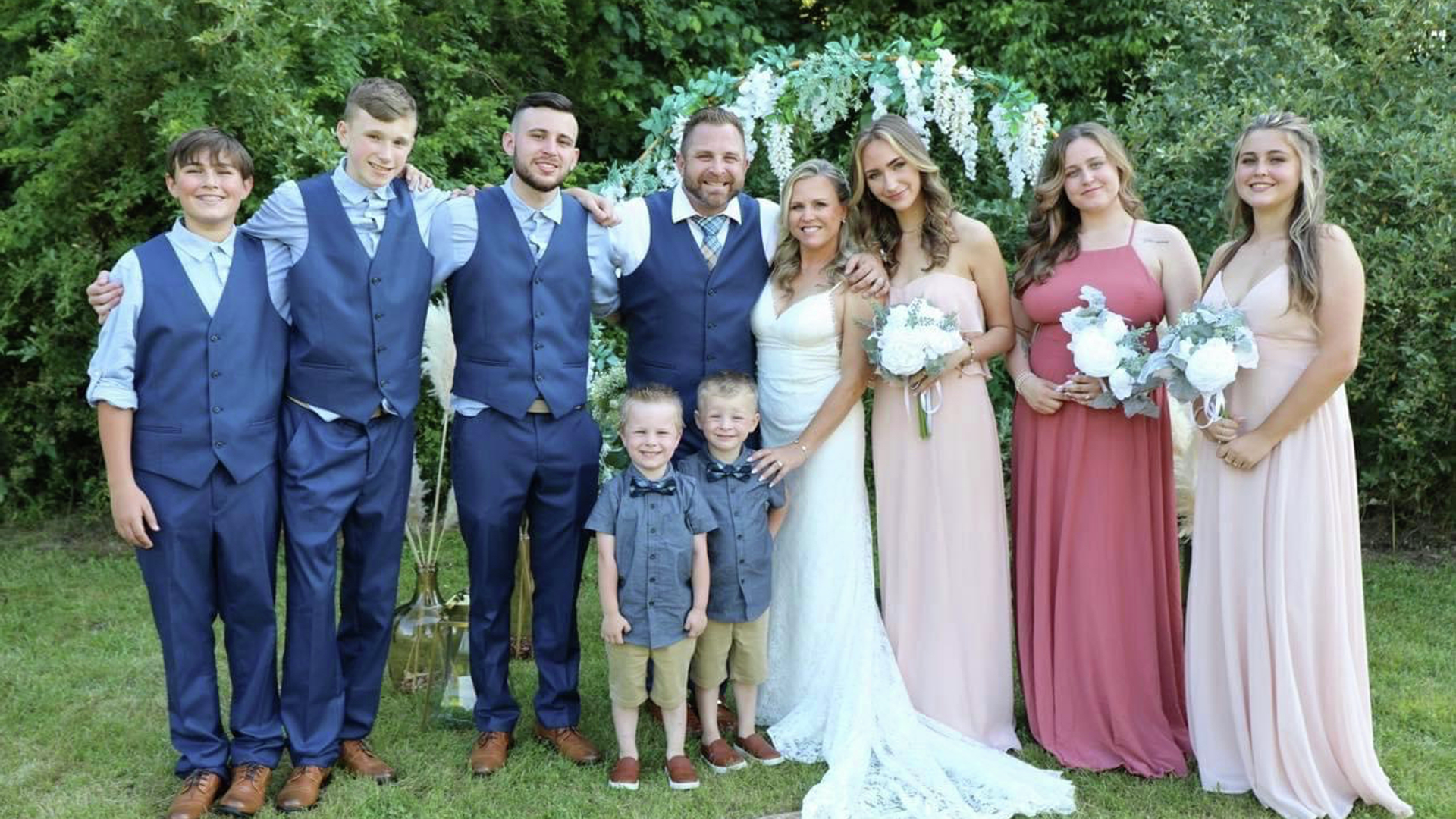 JP and his new bride standing outside with their wedding party on their wedding day.