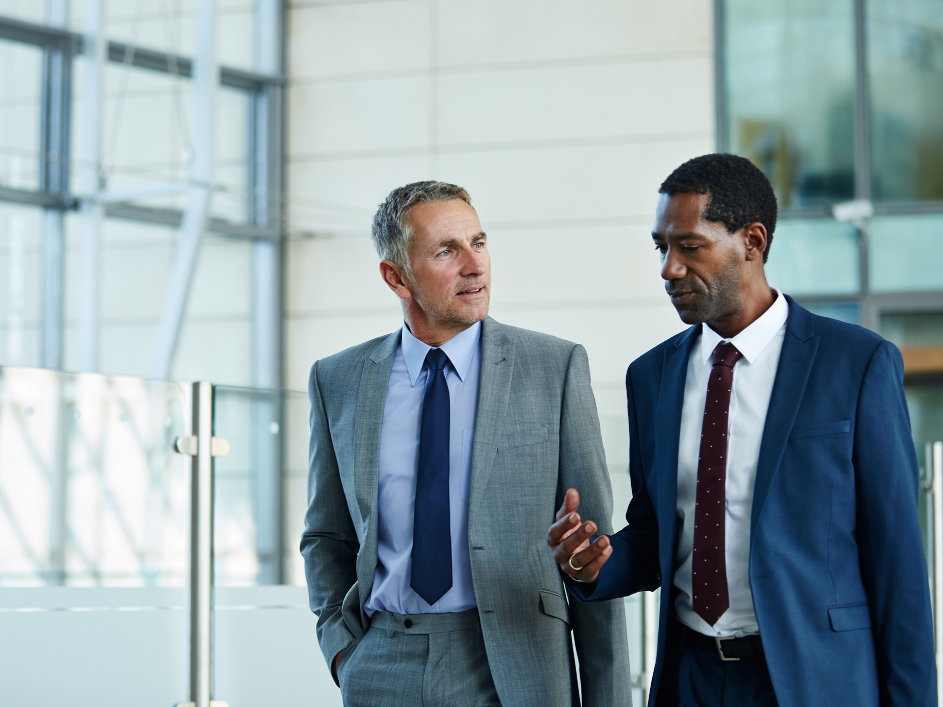 Shot of two businessmen walking and talking together in the lobby of an office building.