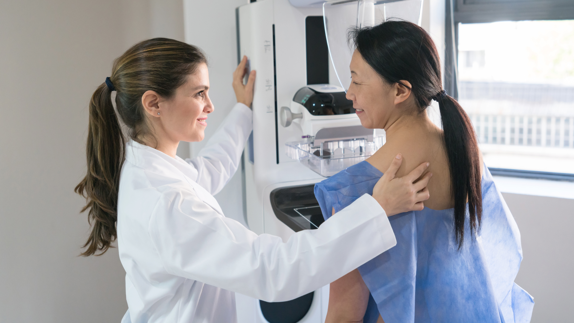 Female gynecologist helping a patient get in position for a mammogram 