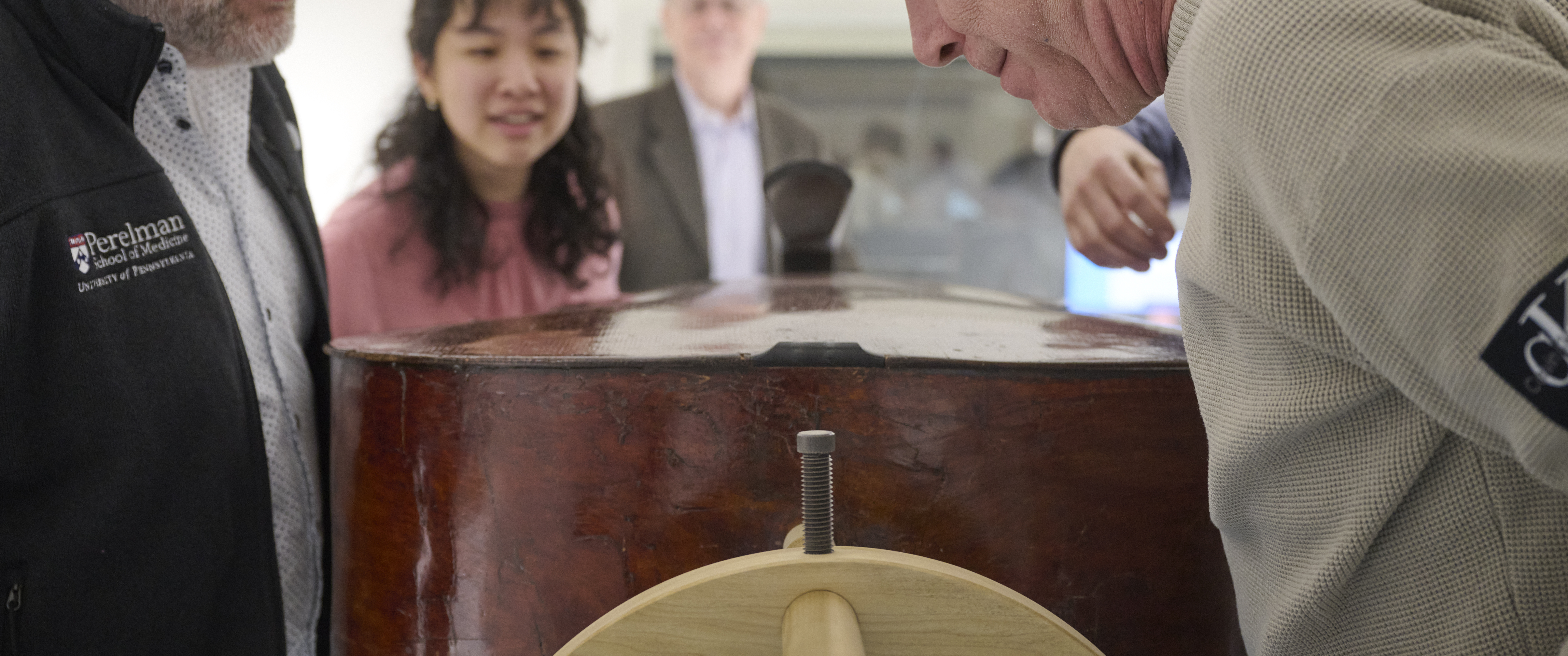 A team of scientists and music experts gathers around a double bass instrument beside a CT scanner