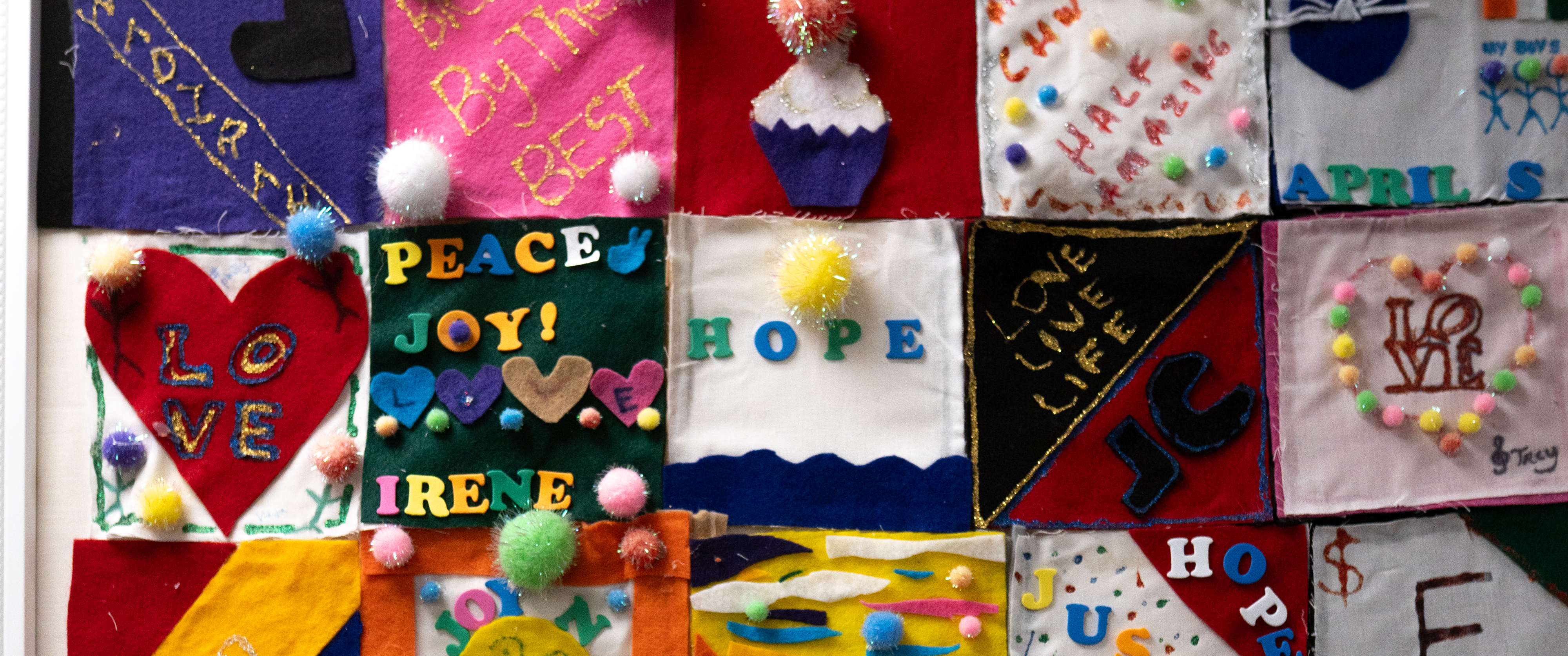 Colorful felt squares featuring words, symbols, and designs including hearts, hope, peace, love and IMPaCT 2019 displayed together on a wall