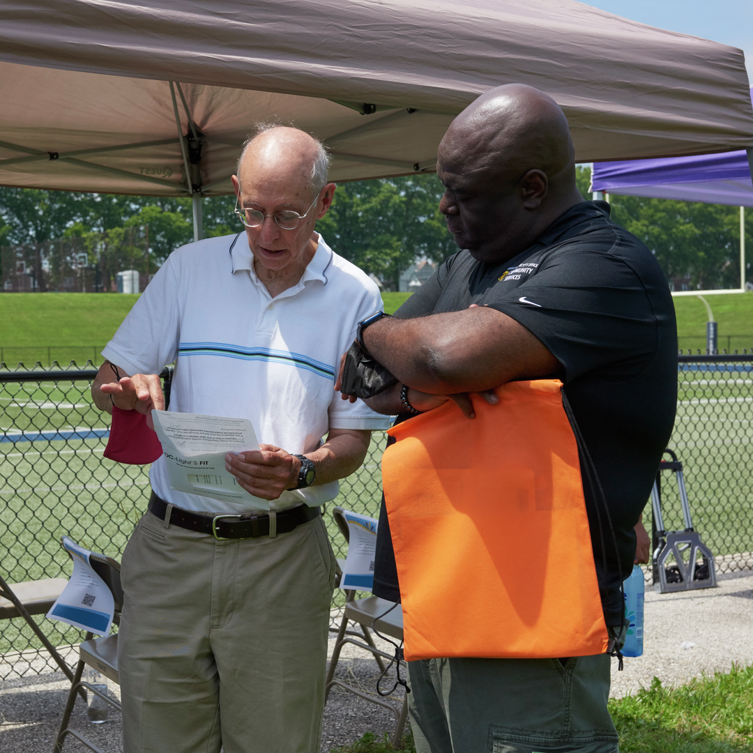 Dr. Michael Goldberg reviews a FIT test kit instructions with a Black man at an outdoor event