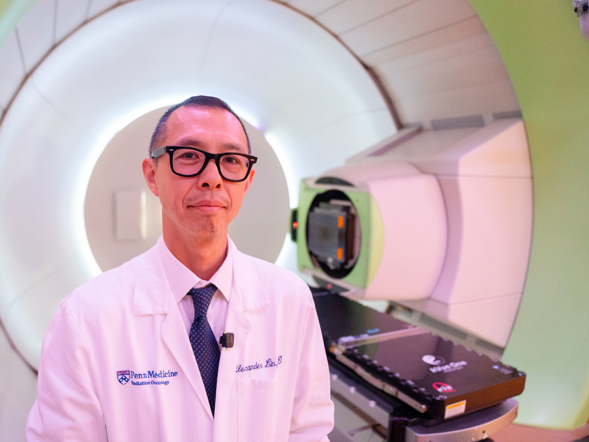 Dr. Alex Lin standing in front of a proton therapy device.