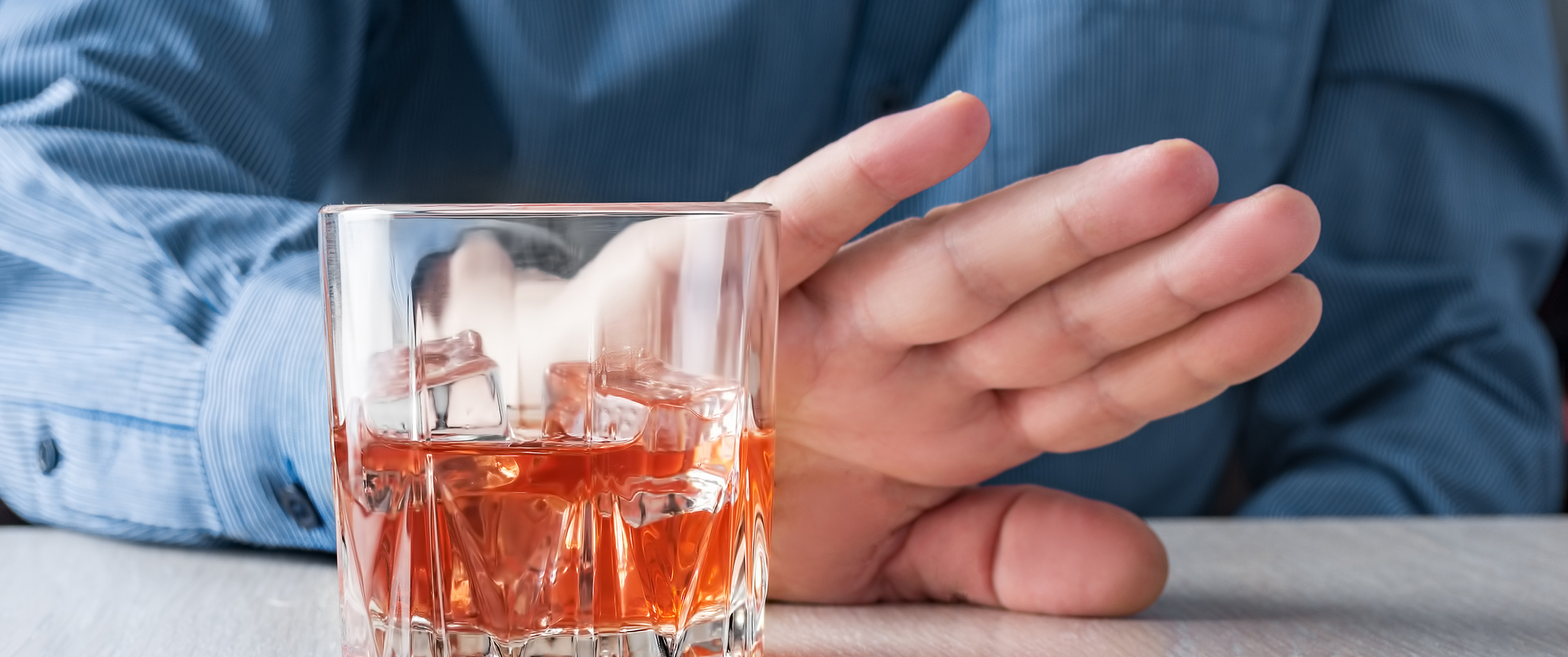 A man holds up a hand to show refusal of taking a glass of alcohol on a table