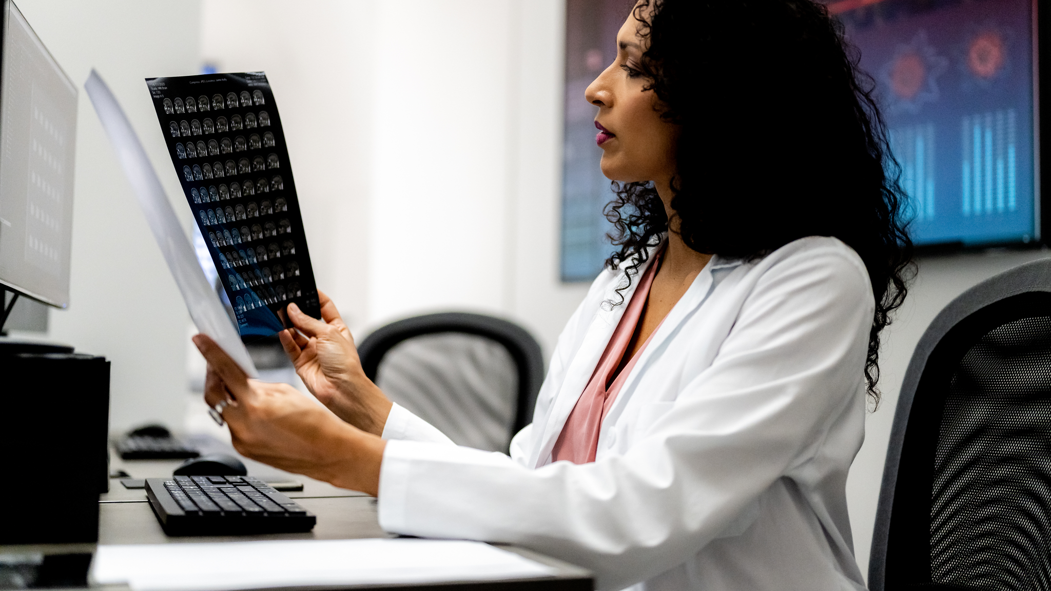 Side view of sitting Hispanic woman. Radiologist comparing magnetic resonance imaging results. 