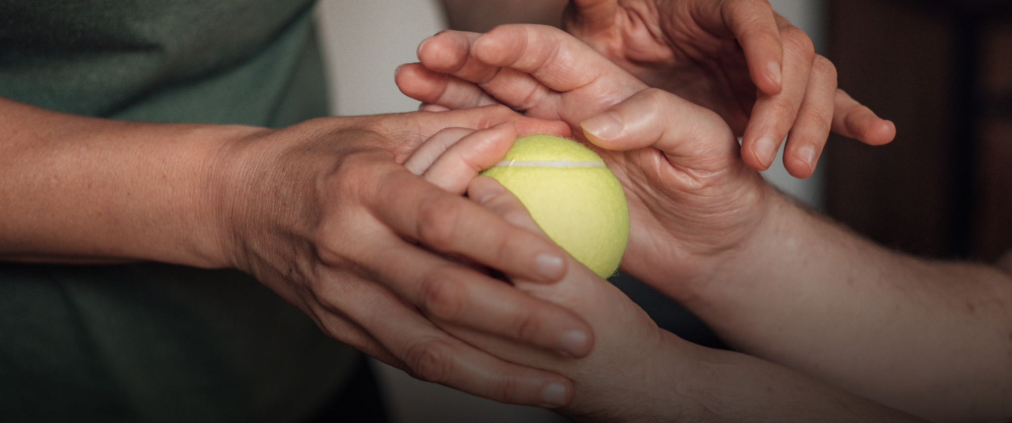Luka Krizanac’s hands holding a tennis ball, while his physical therapist is holding his hands in hers