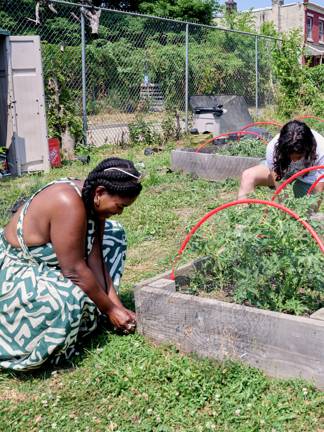 Two people kneel beside a raised planter bed and may be weeding