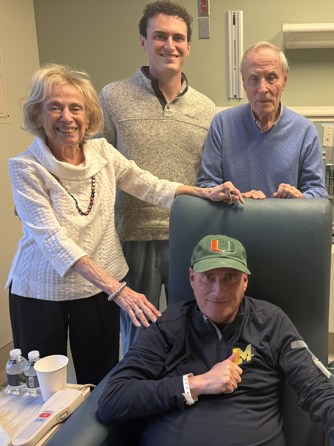 Curt Krouse sits in an infusion chair receiving gene therapy surrounded by his smiling parents and young adult son