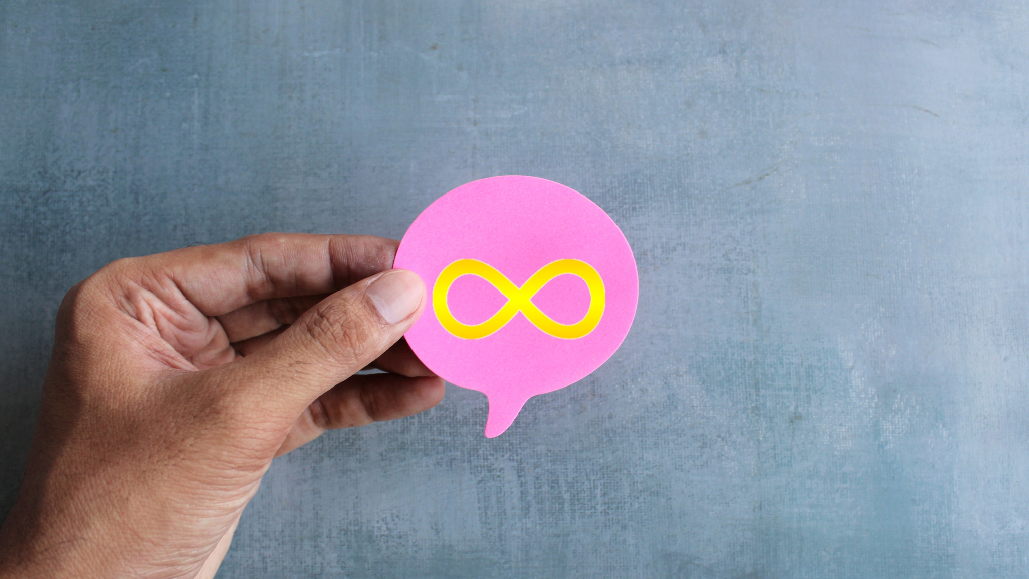 A hand holding a speech bubble with a gold infinity symbol in its center