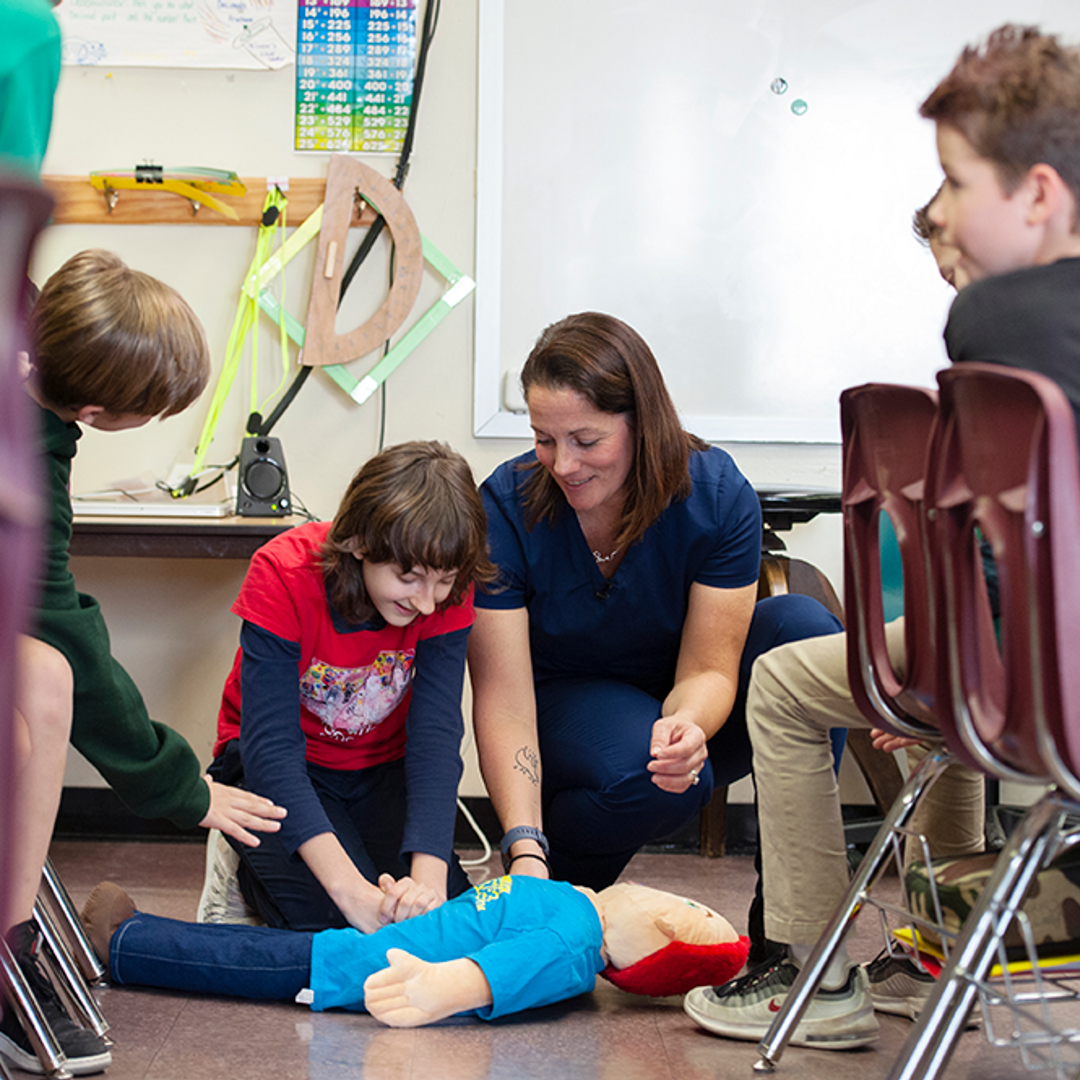 Sara Cohen helps an elementary school student practice the Heimlich maneuver on a training doll