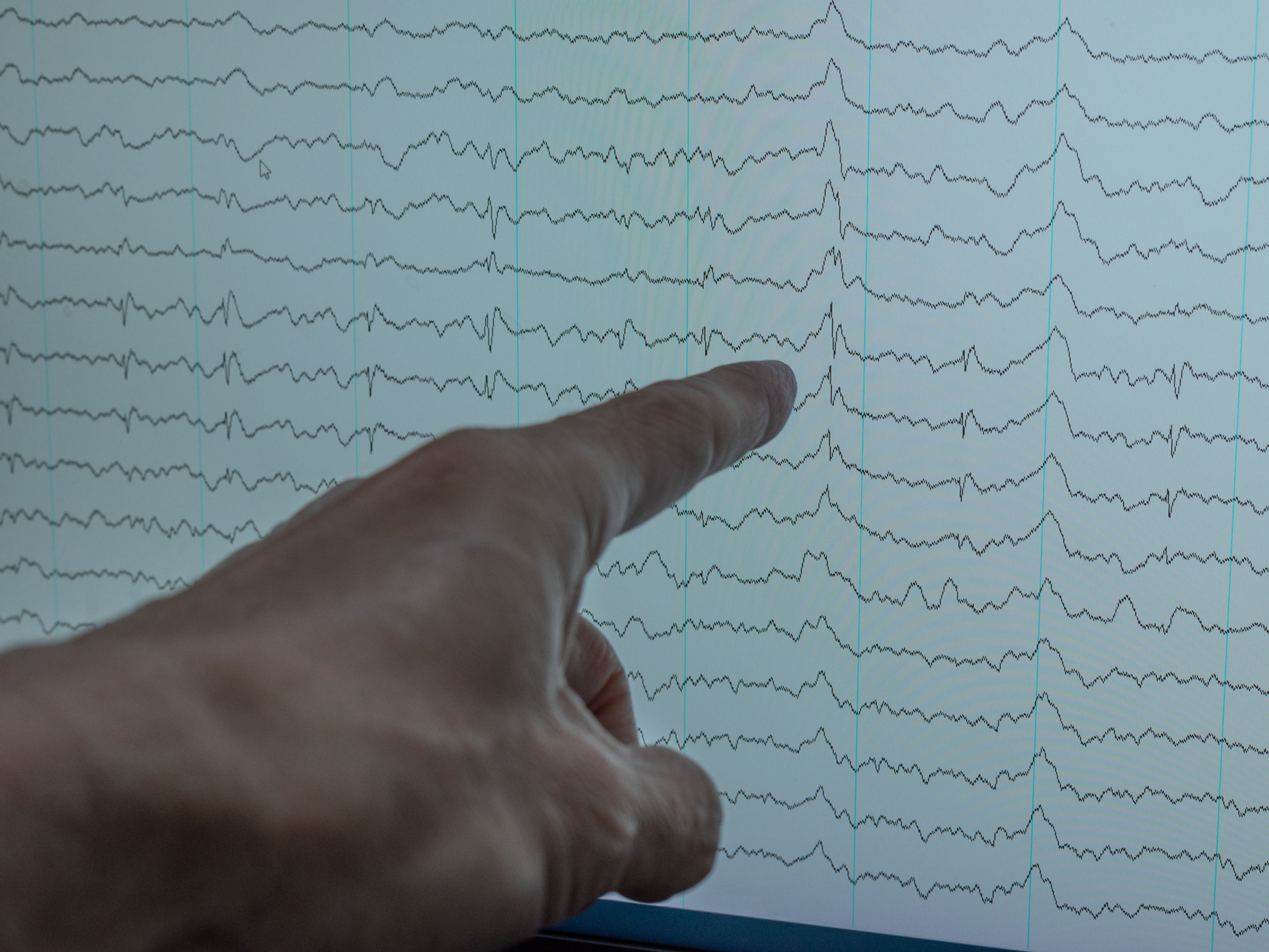A hand pointing at EEG graph on screen, analyzing brainwave patterns