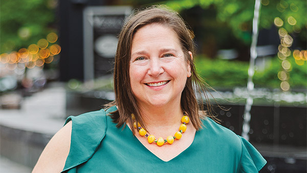 Portrait of Christy Hofmanner outdoors wearing green top and orange beaded necklace