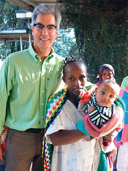 Albert Ruenes standing with his arm around a mother holding a baby wrapped in colorful blankets.