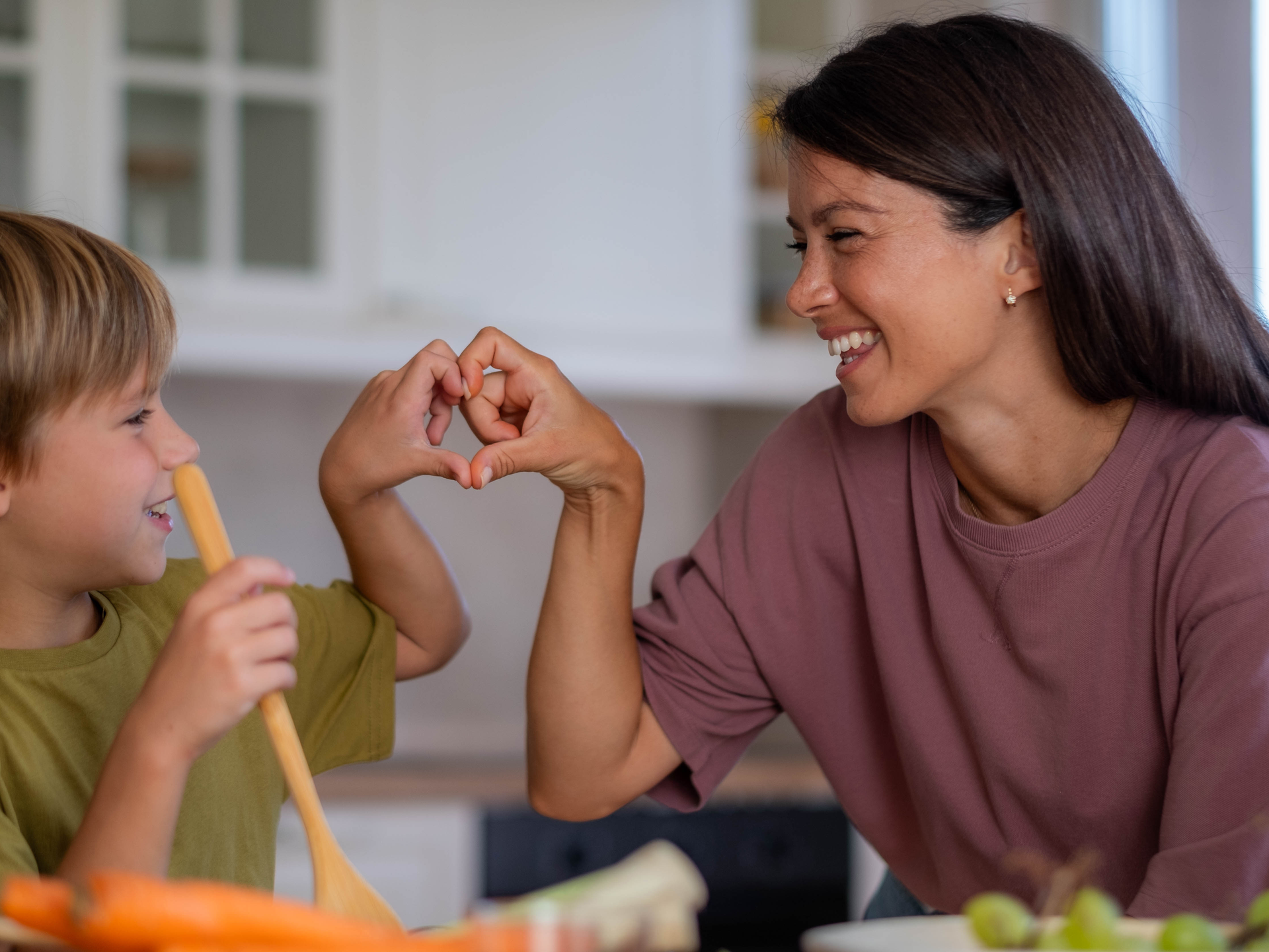 Happy mom and son in the kitchen preparing food and making a heart shape with their hands