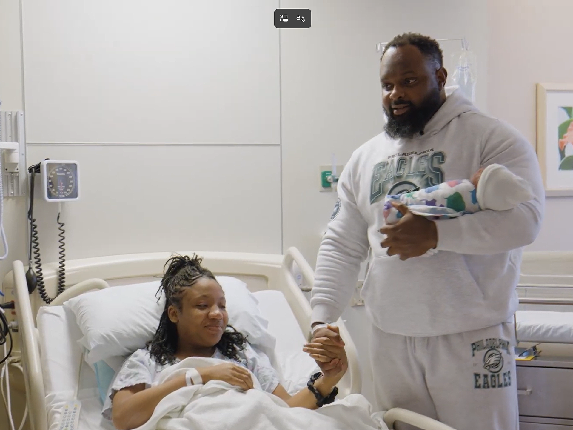 Father holding a baby next his wife resting on a maternity bed