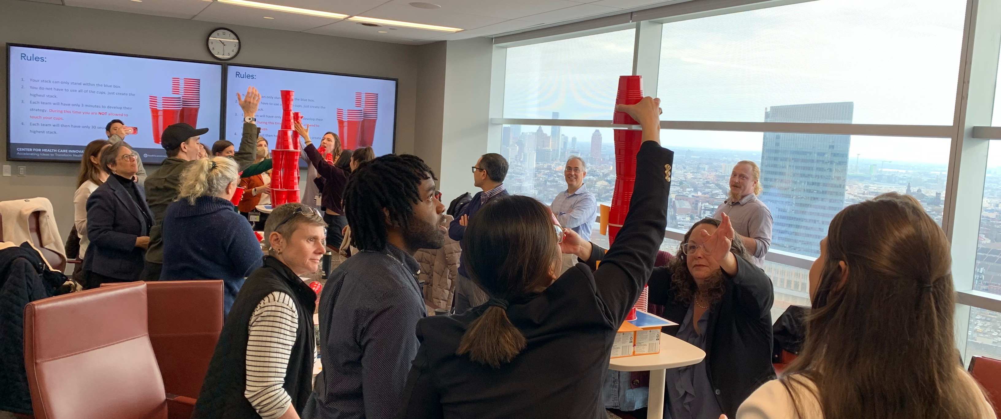 Two competing groups in a conference room create towers of red plastic cups in a design exercise