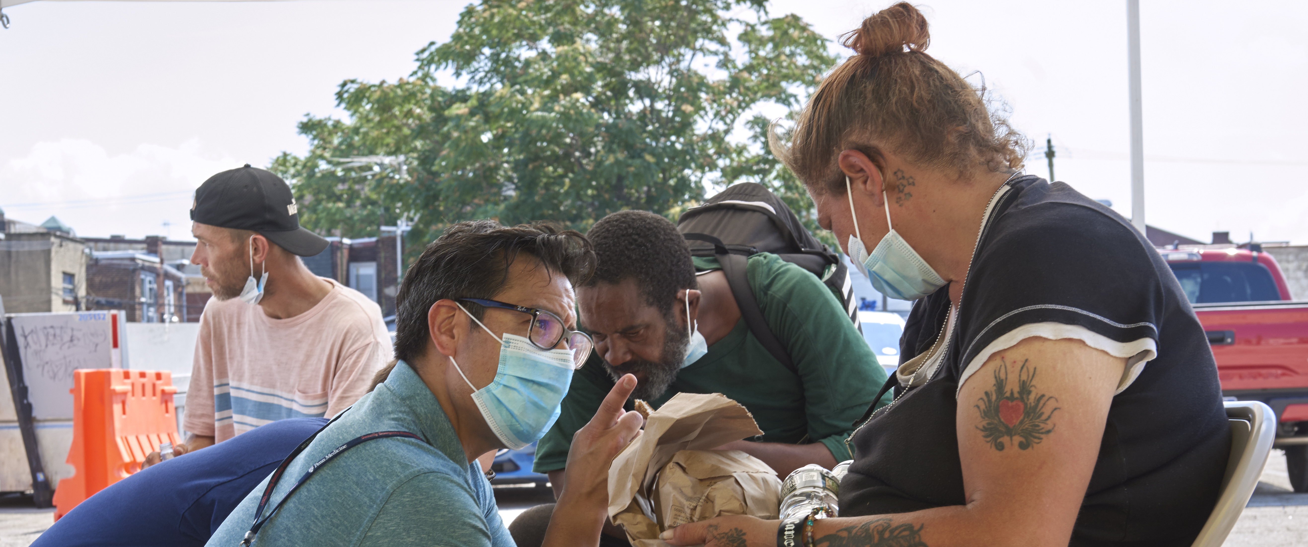 Antonio Davila kneels talking with one of several people seated in folding chairs under a tent