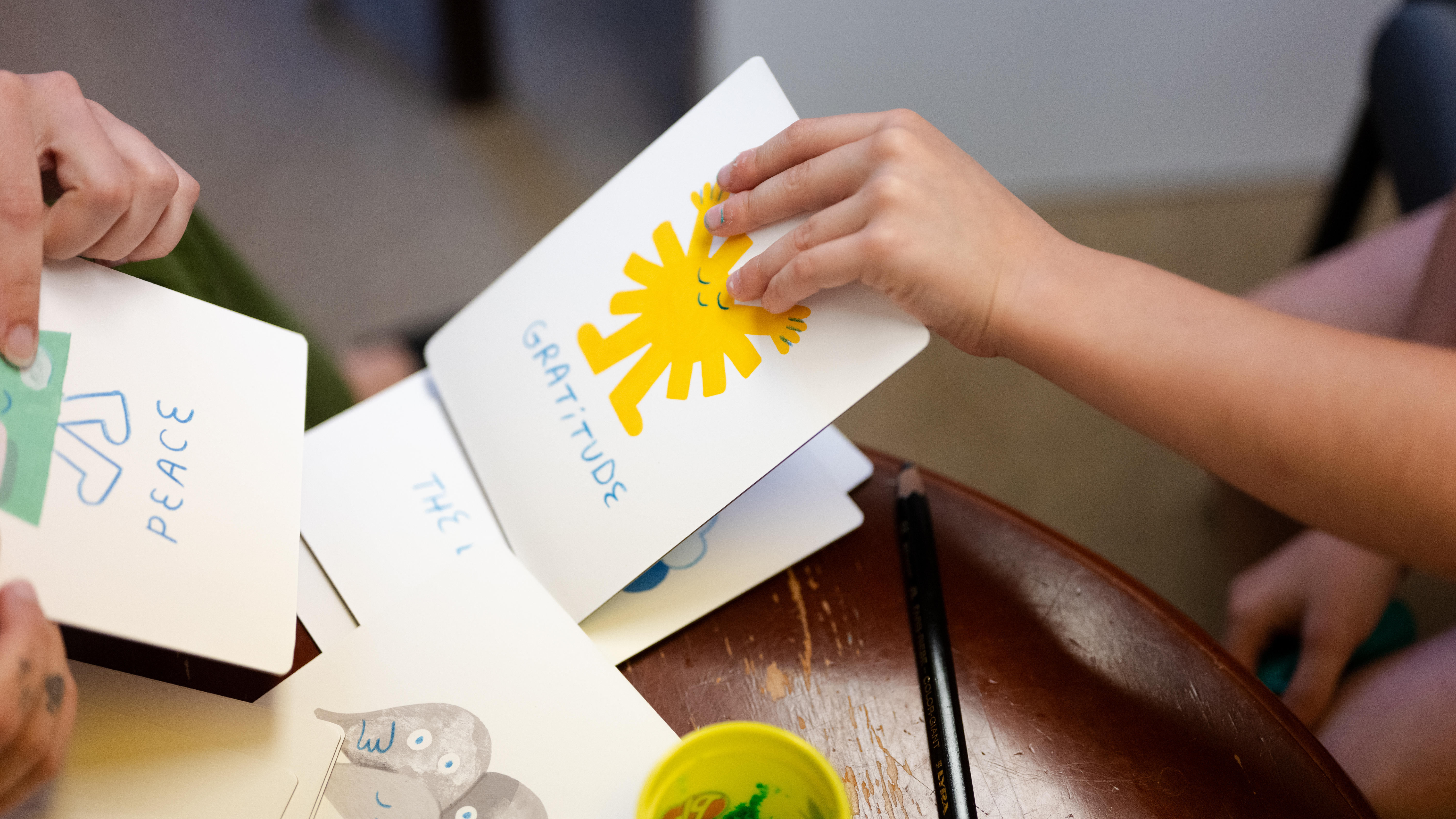 Close up on the hands of a therapist and a child, holding cards displaying emotions