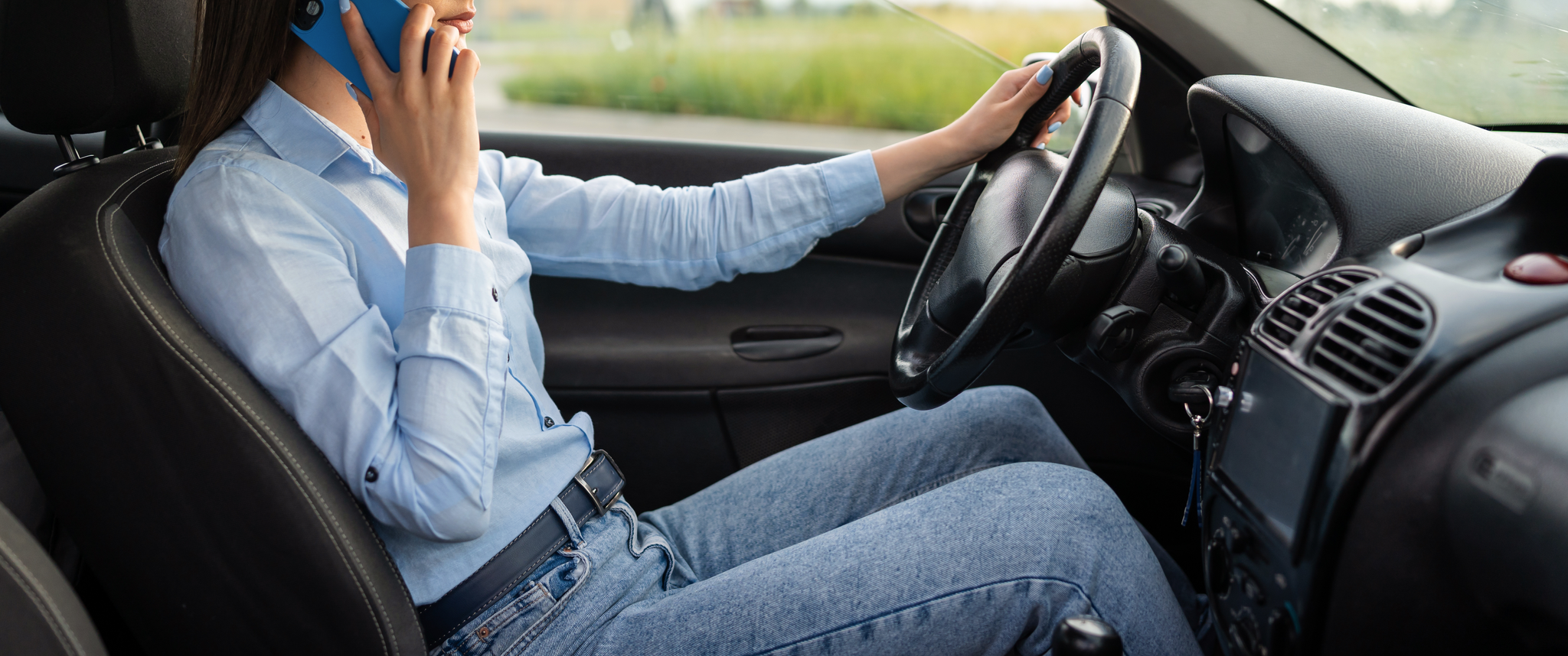 A woman, who is driving a car, holds a cell phone in one hand for a call