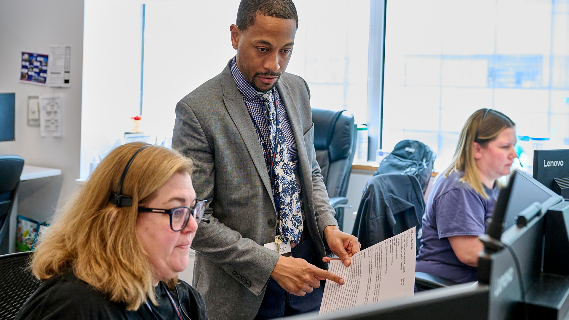 Joshua Davis stands, discussing a document with two seated nurses wearing headsets