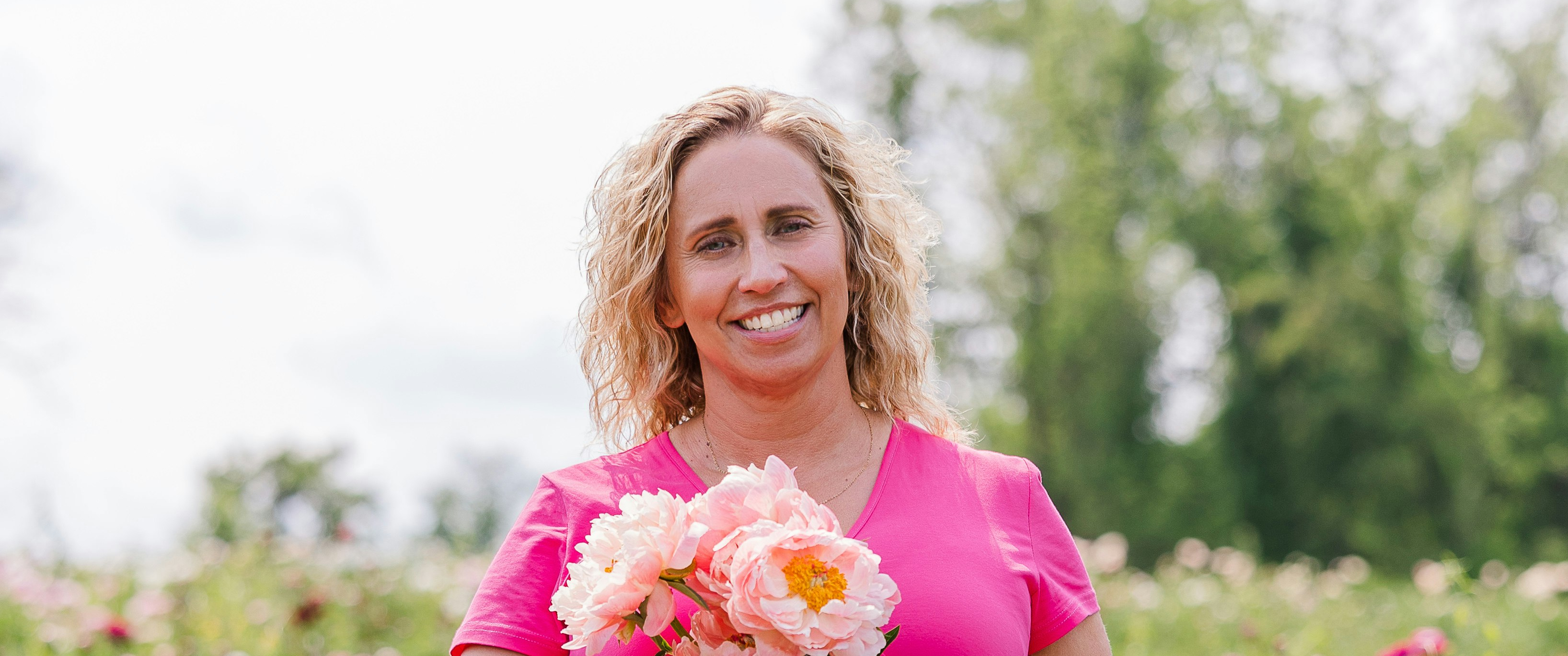  Karen Tarbotton standing in a field of flowers in a pink dress, holding a bouquet of blooming roses