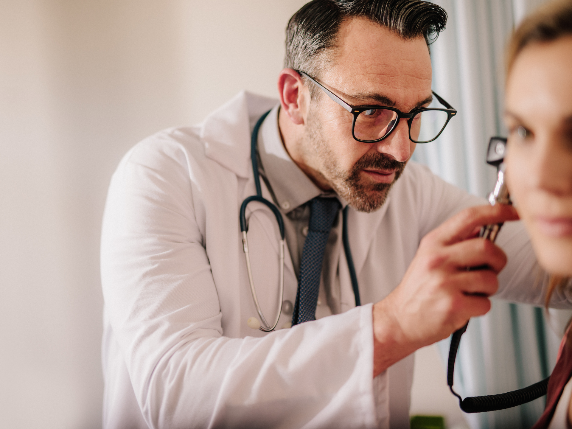 Male doctor looking at female patient's ear through otoscope