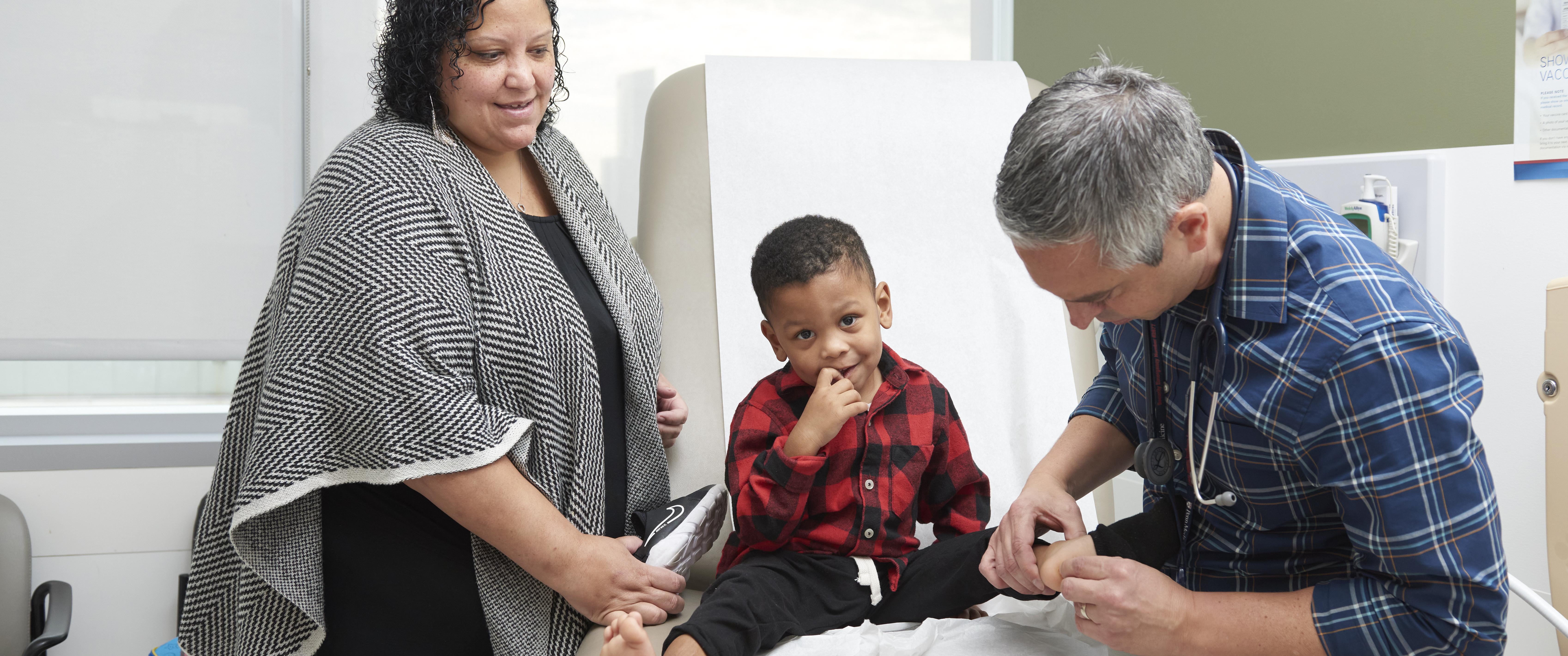 Nicole Miller stands beside an exam table where her 3-year-old son is being examined by physician Mario DeMarco, MD