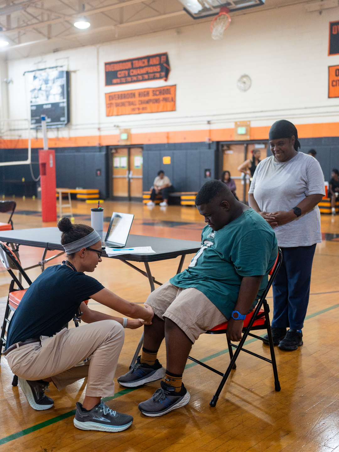 Brandy Hennie standing next to her son Jaisen Smith as he undergoes a sports physical in a school gym