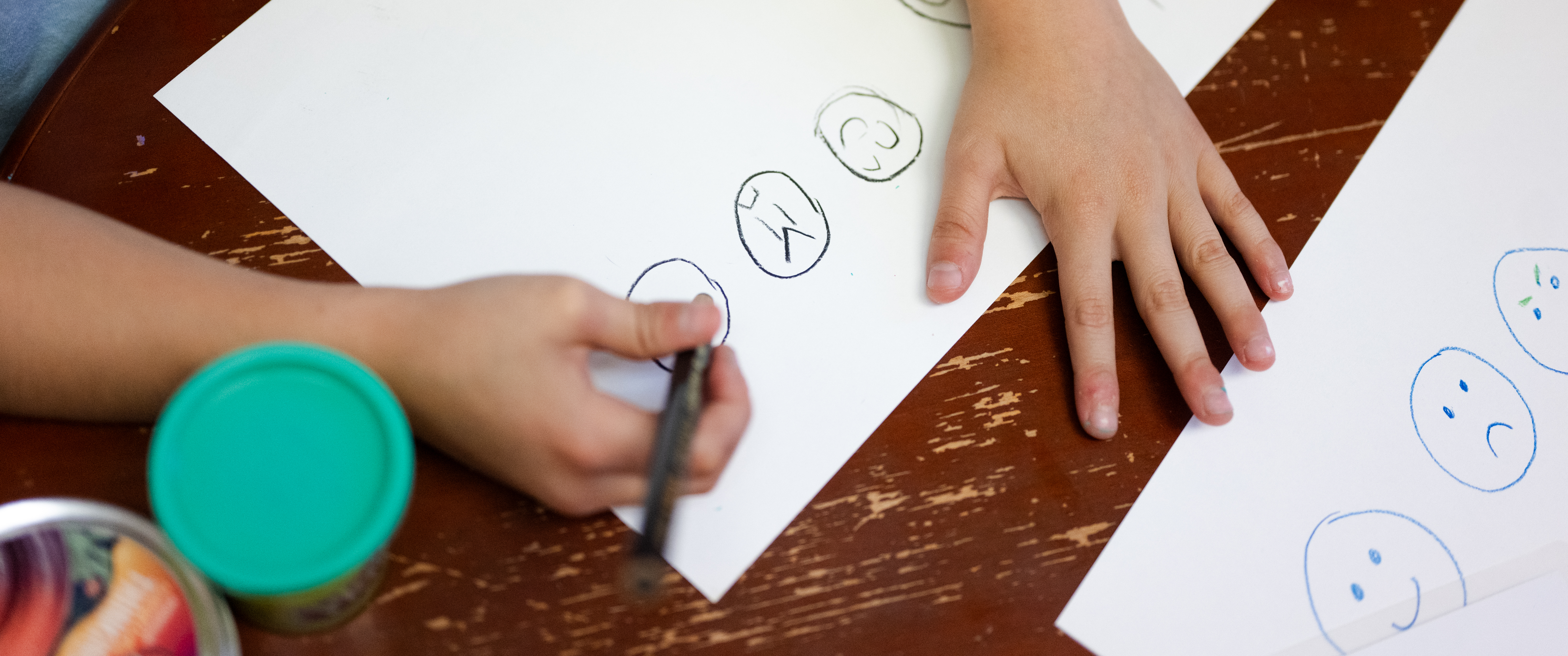 A child draws pictures of faces on a sheet of paper