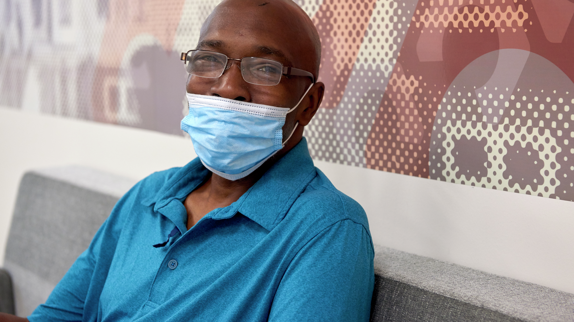 Nathaniel Williams, a 59-year-old Black man, is smiling behind a surgical mask while sitting in a waiting room