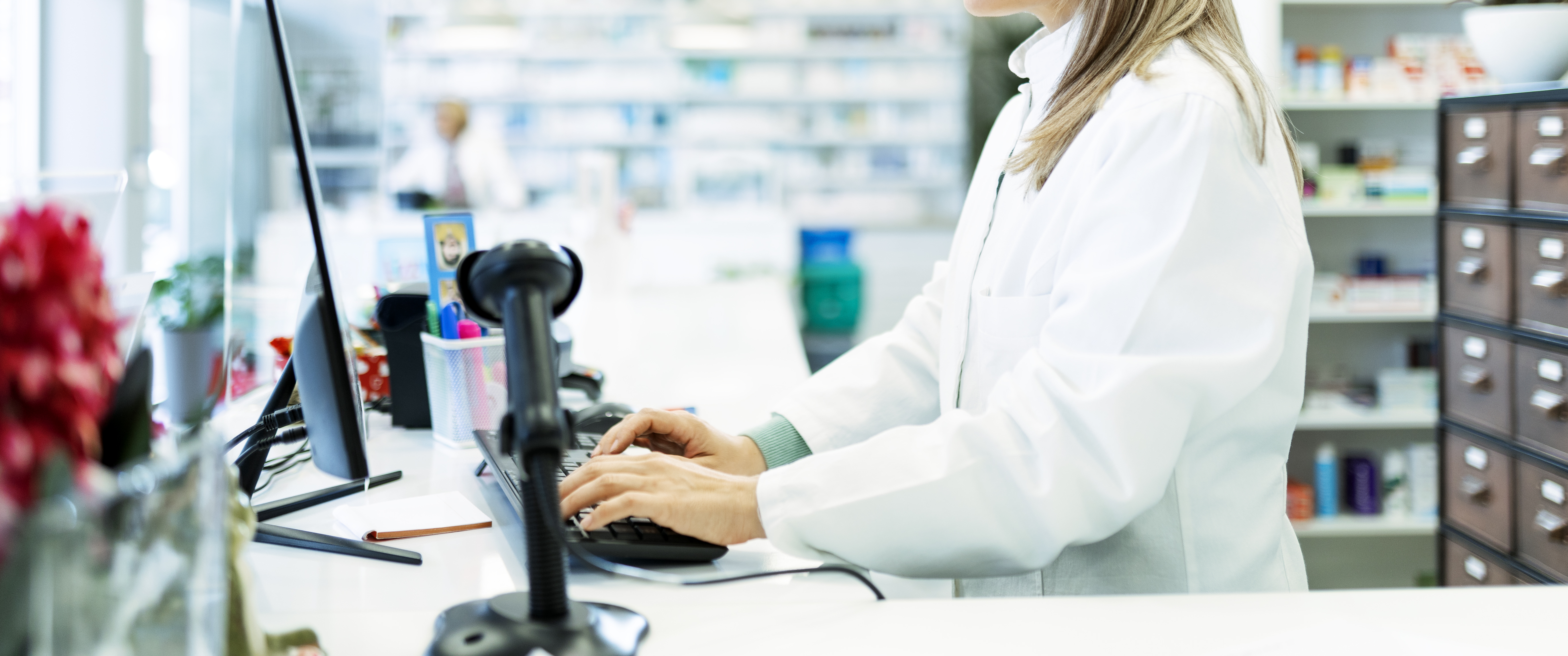 A pharmacist typing on the computer behind the counter of a drugstore 