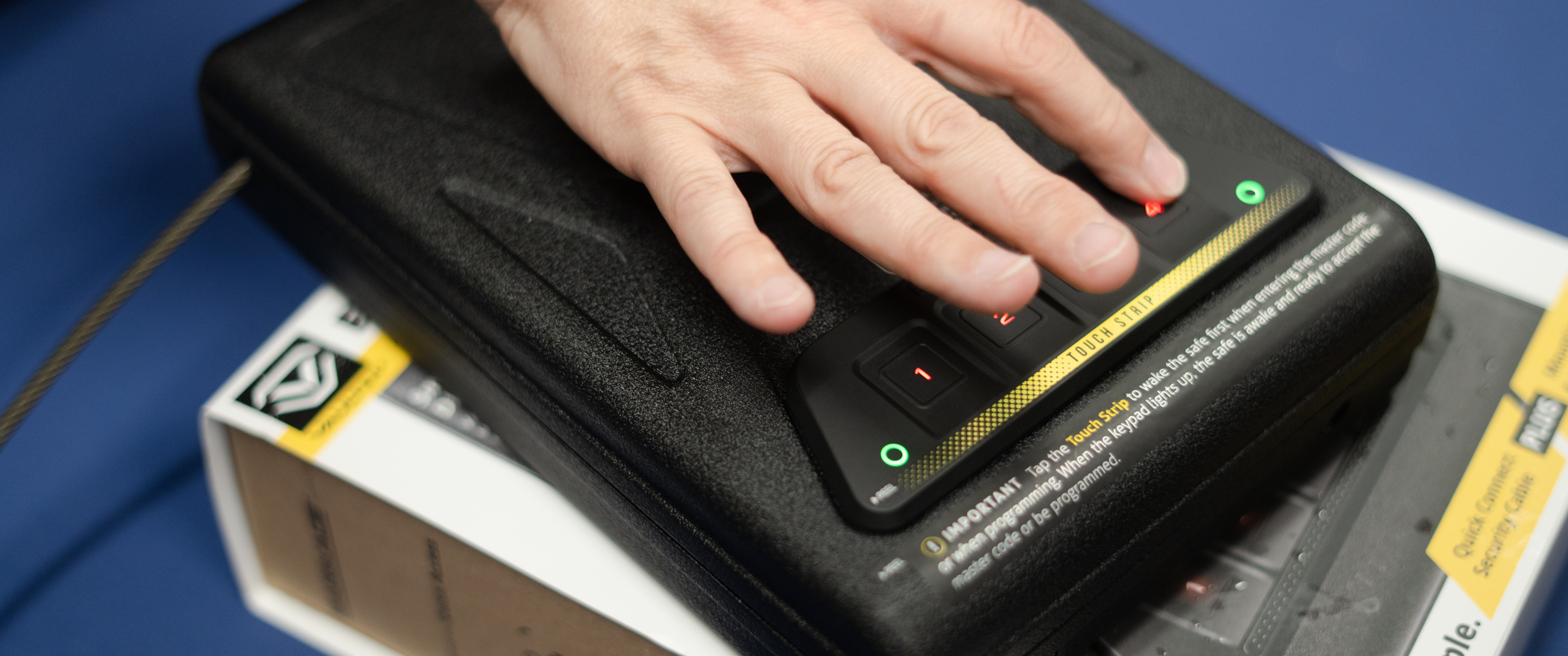 Sunny Vespico demonstrates how to open a black gun lockbox. Her hand hovers over a row of numbers, her index finger is pressing buttons to enter the combination to open the lockbox.