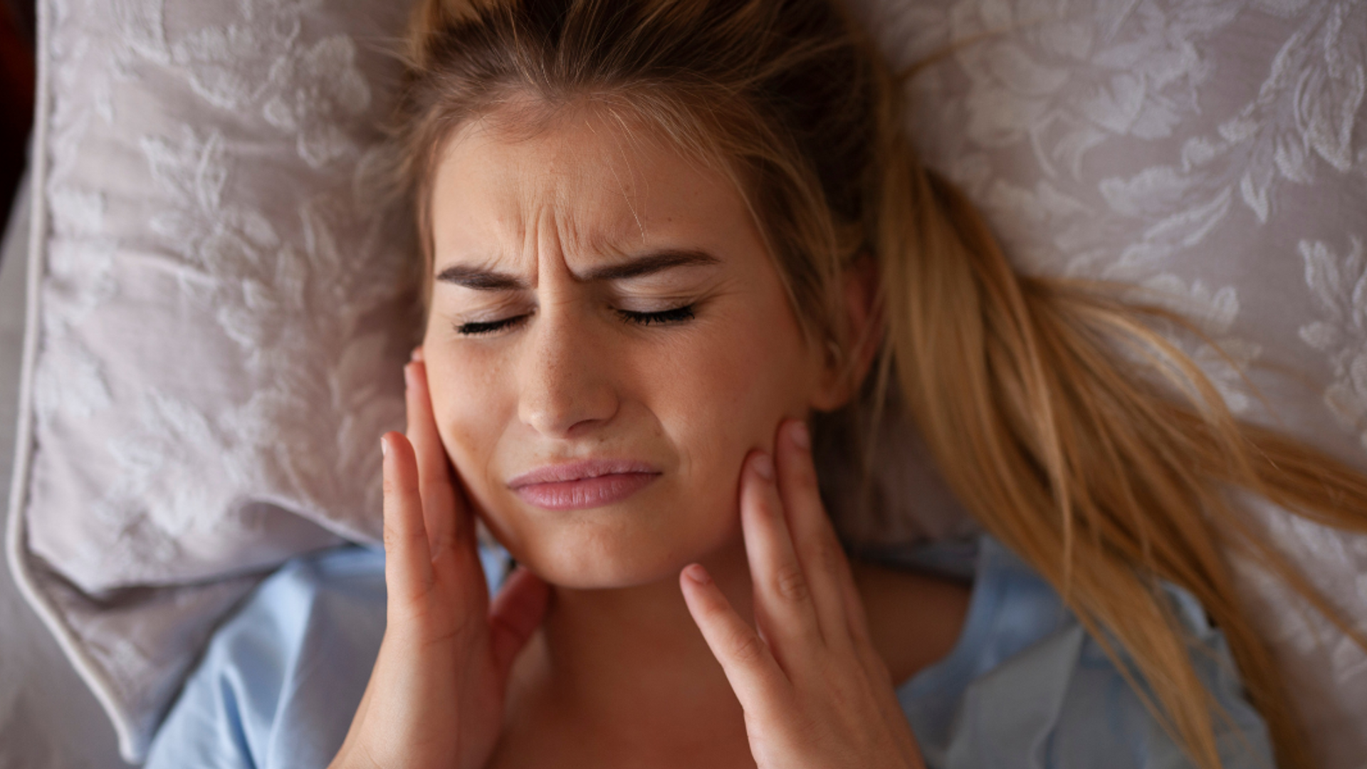 Woman lying on pillow in pain with hands touching jaw