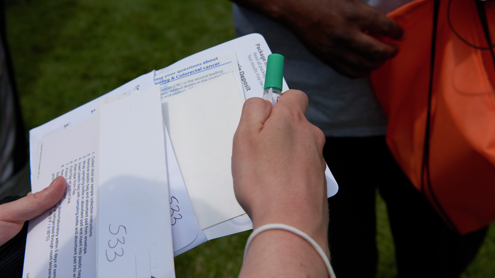 Close-up of a woman's hands with an envelope that lists instructions for collecting a stool sample, as well as a plastic vial