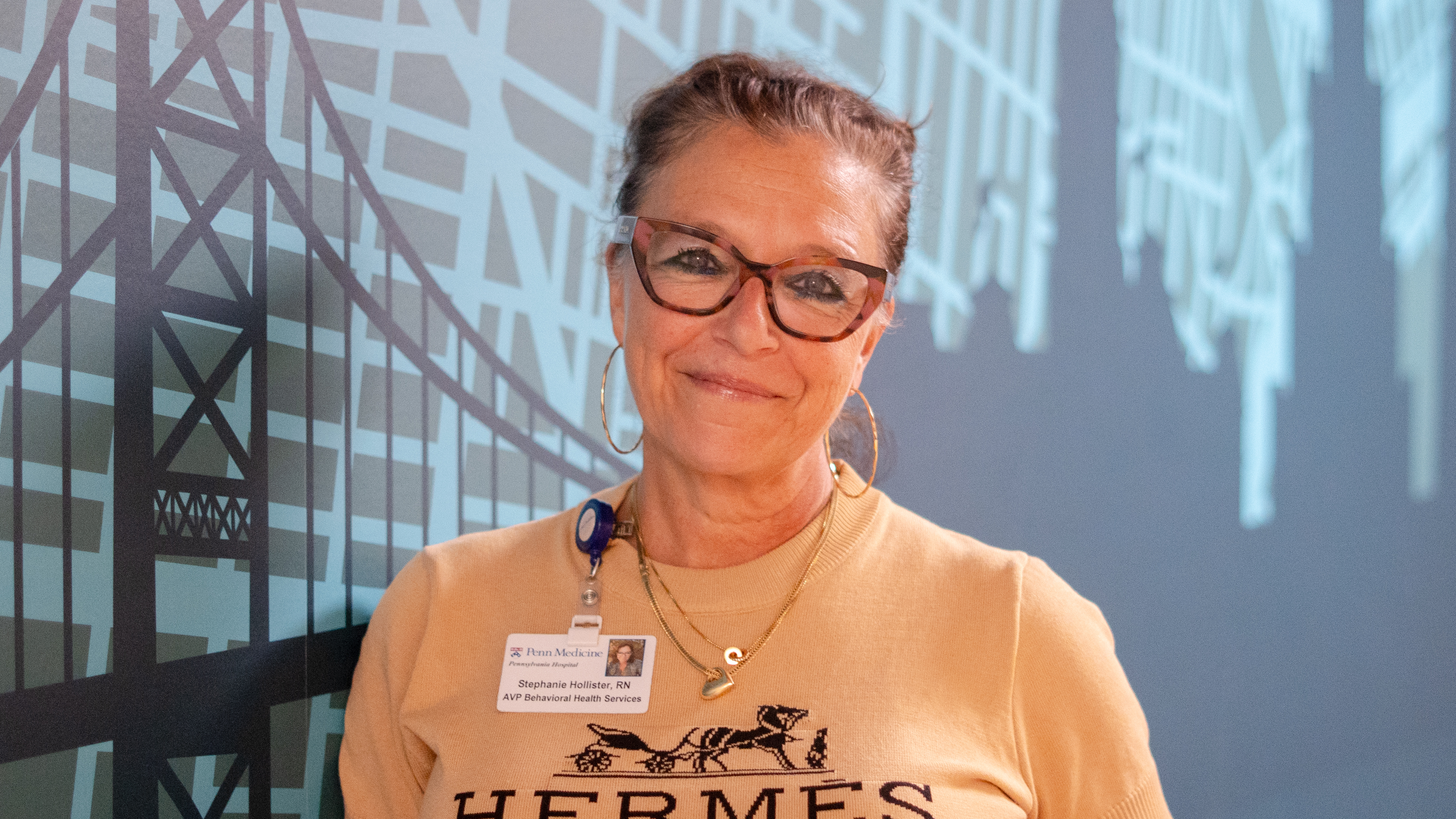 Female staff member poses in front of a mural of Philadelphia in an inpatient space