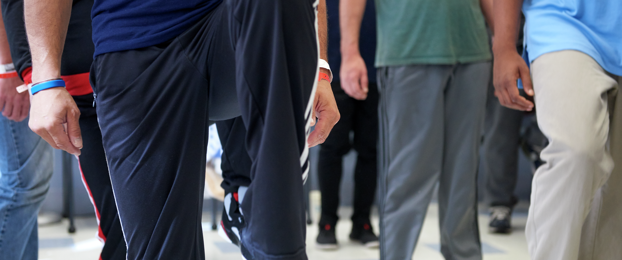 The arms and legs of men wearing comfortable clothing with medical bracelets, standing and doing leg lifts