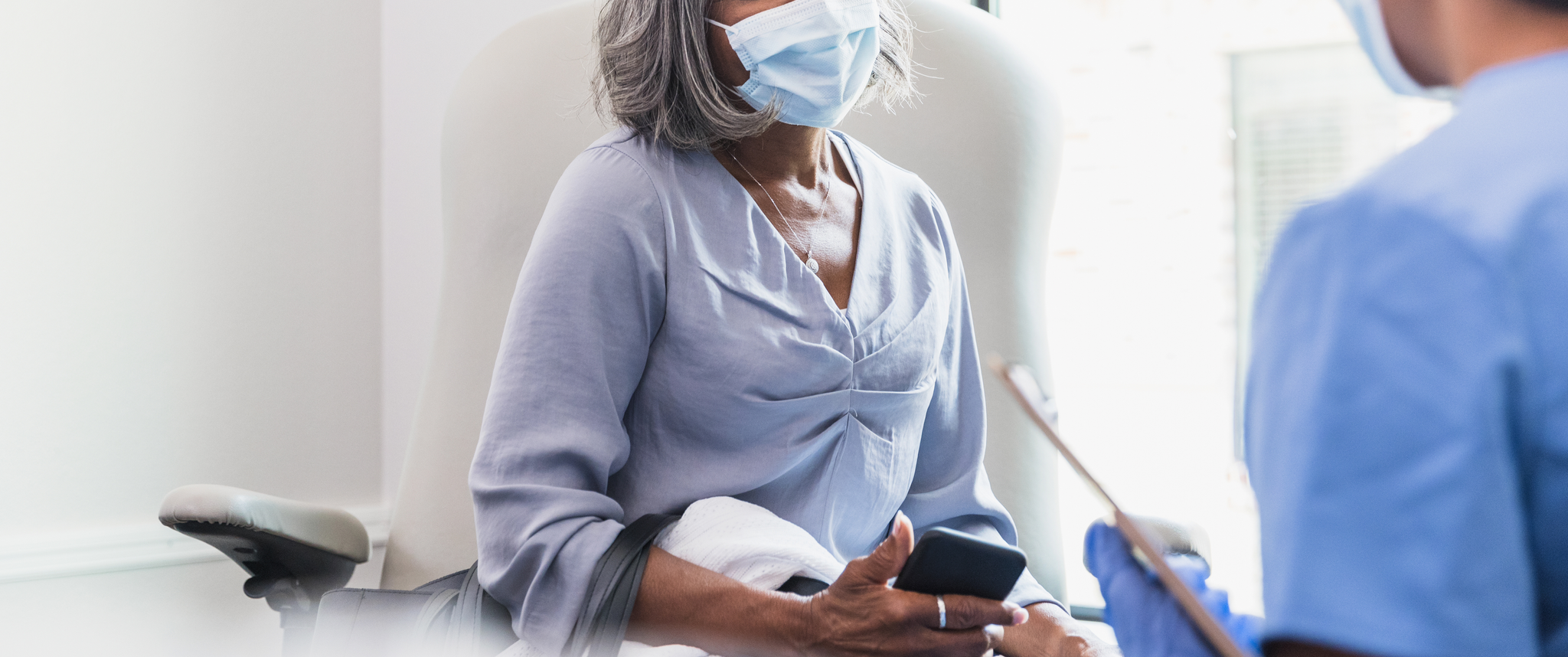 A woman wearing a mask meets with a doctor in a patient room
