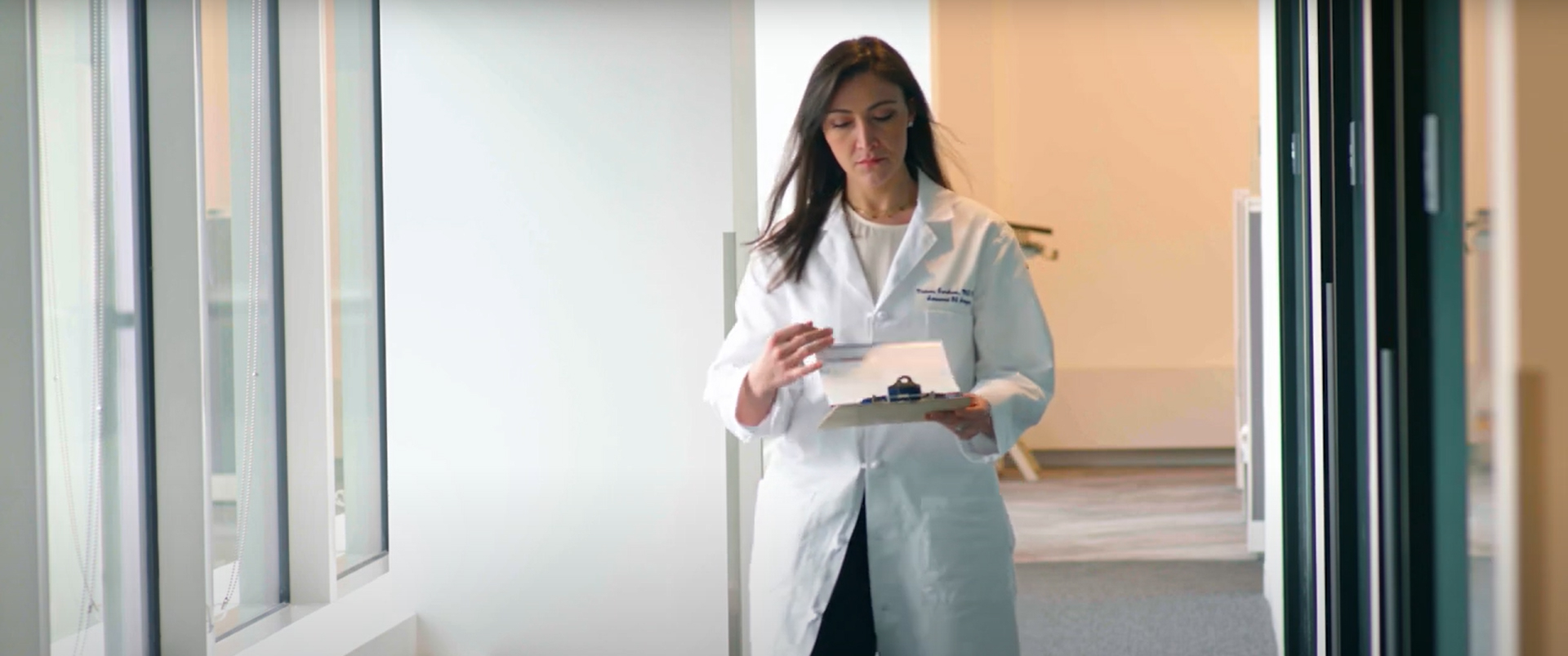 Victoria Gershuni, MD, in a white lab coat, looking at a clipboard while walking down a hallway