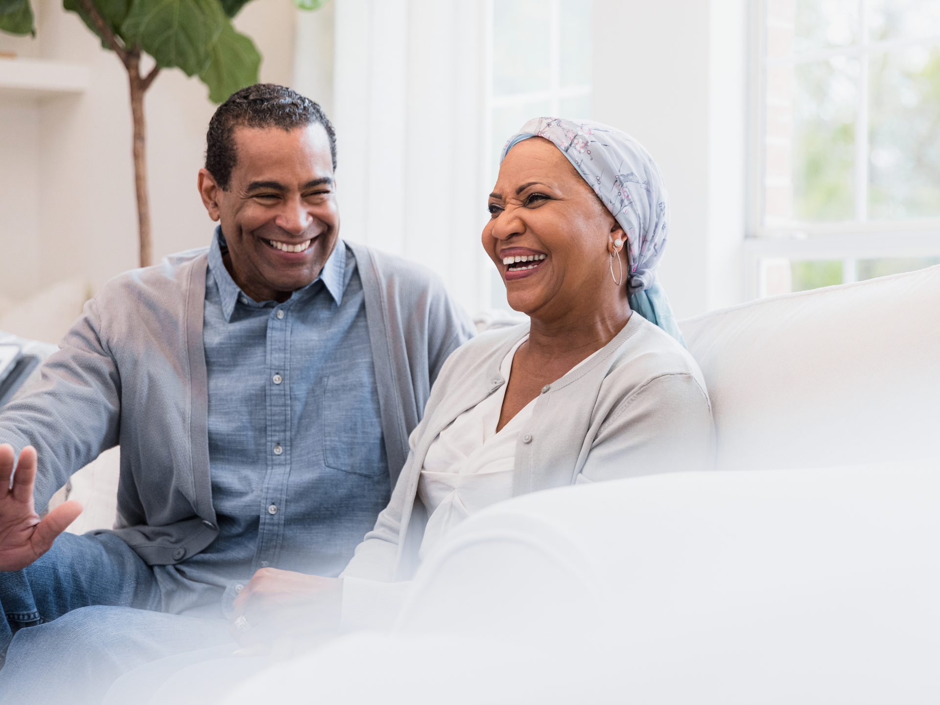 Sitting on their sofa at home, the senior adult couple smiles and laughs at a joke