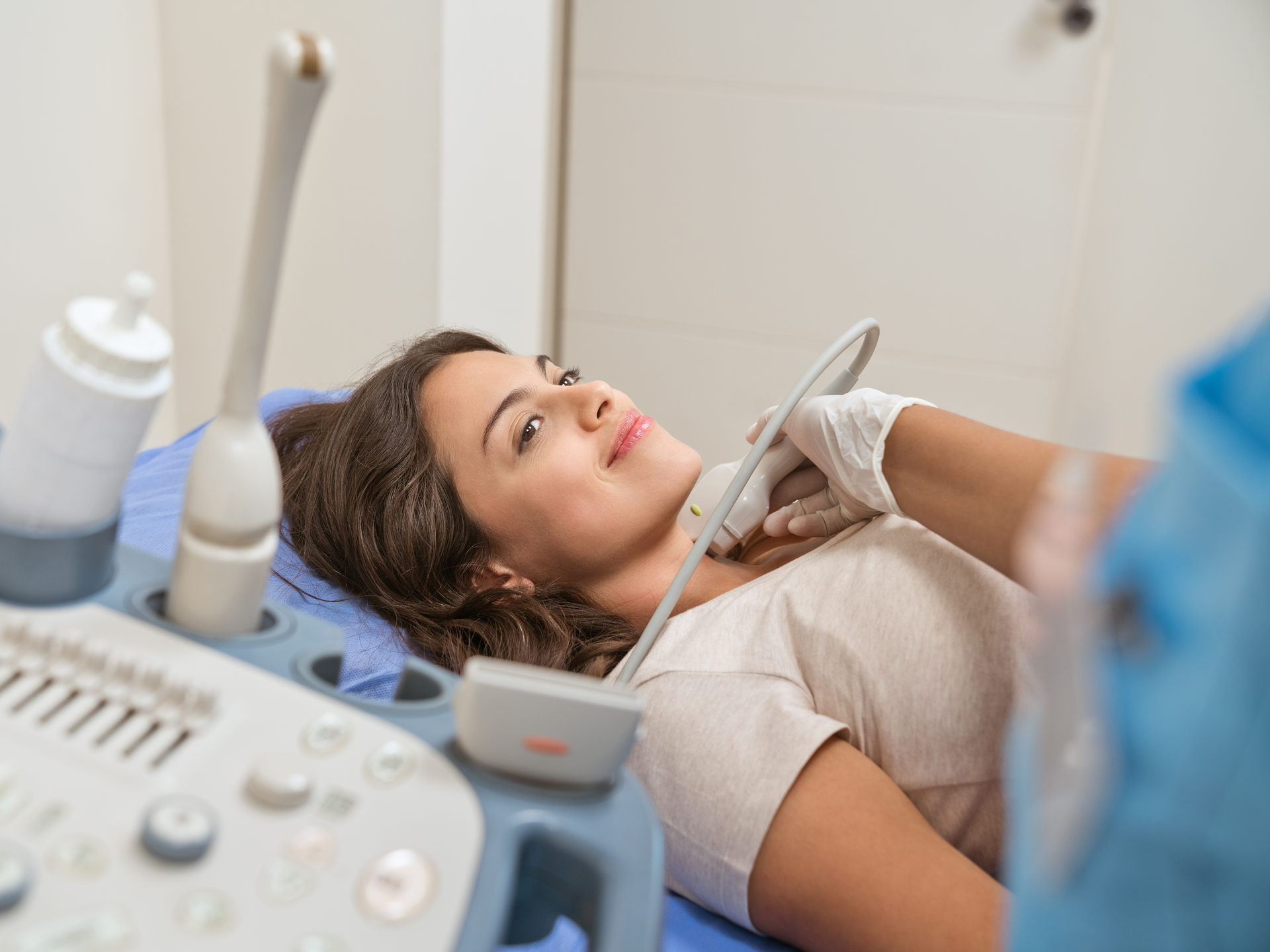A female patient laying down and looking towards her doctor as she receives an ultrasound of her thyroid.