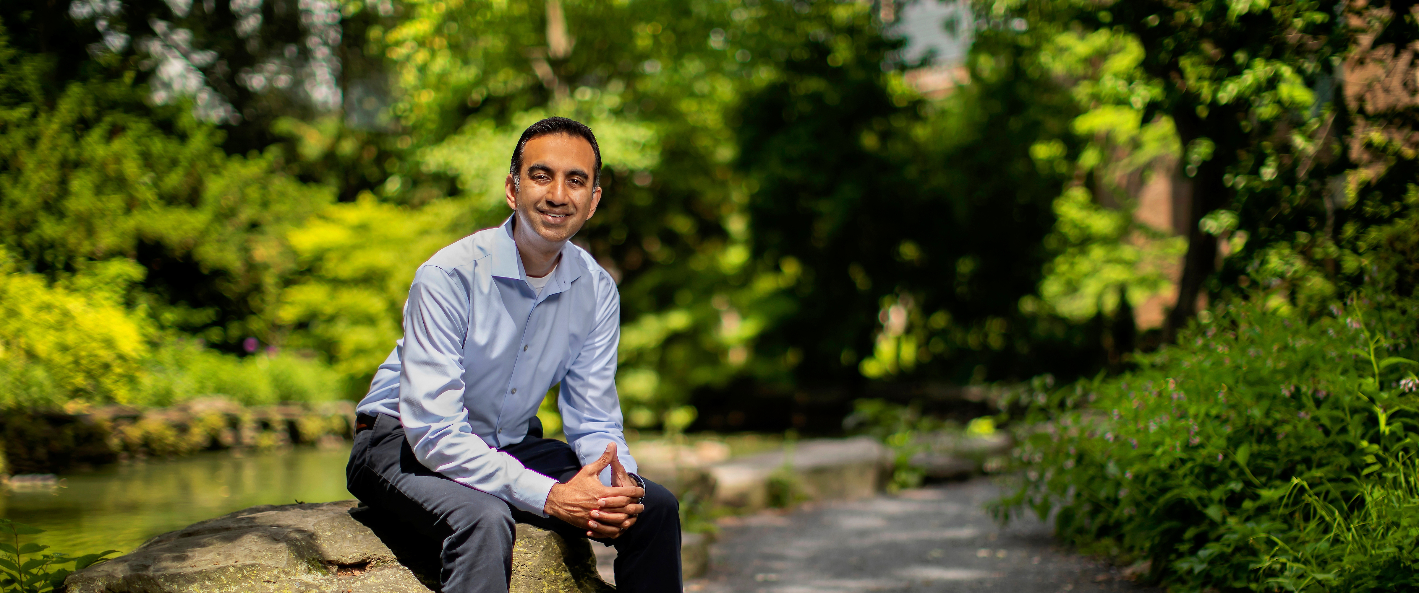  Amol Navathe, MD, PhD, sitting in a park with trees in the background