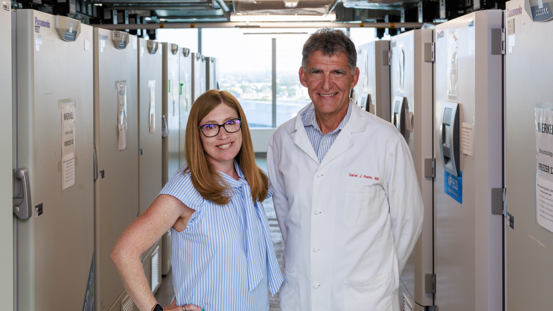 Marylyn Ritchie and Daniel Rader stand together in front of a long row of BioBank specimen freezers