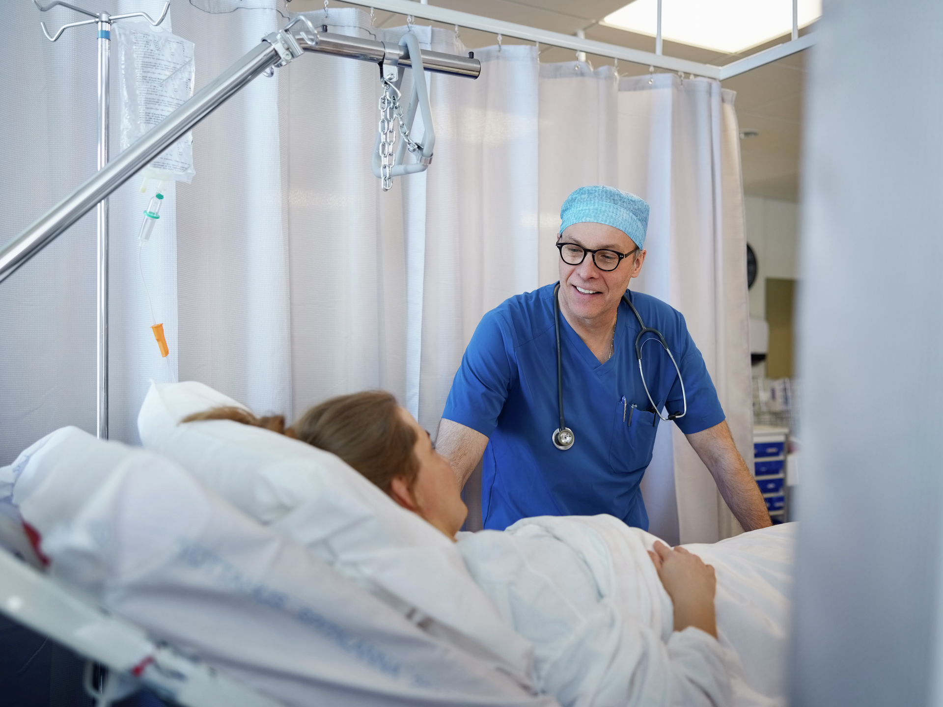 Happy doctor talking and examining patient on bed after surgery