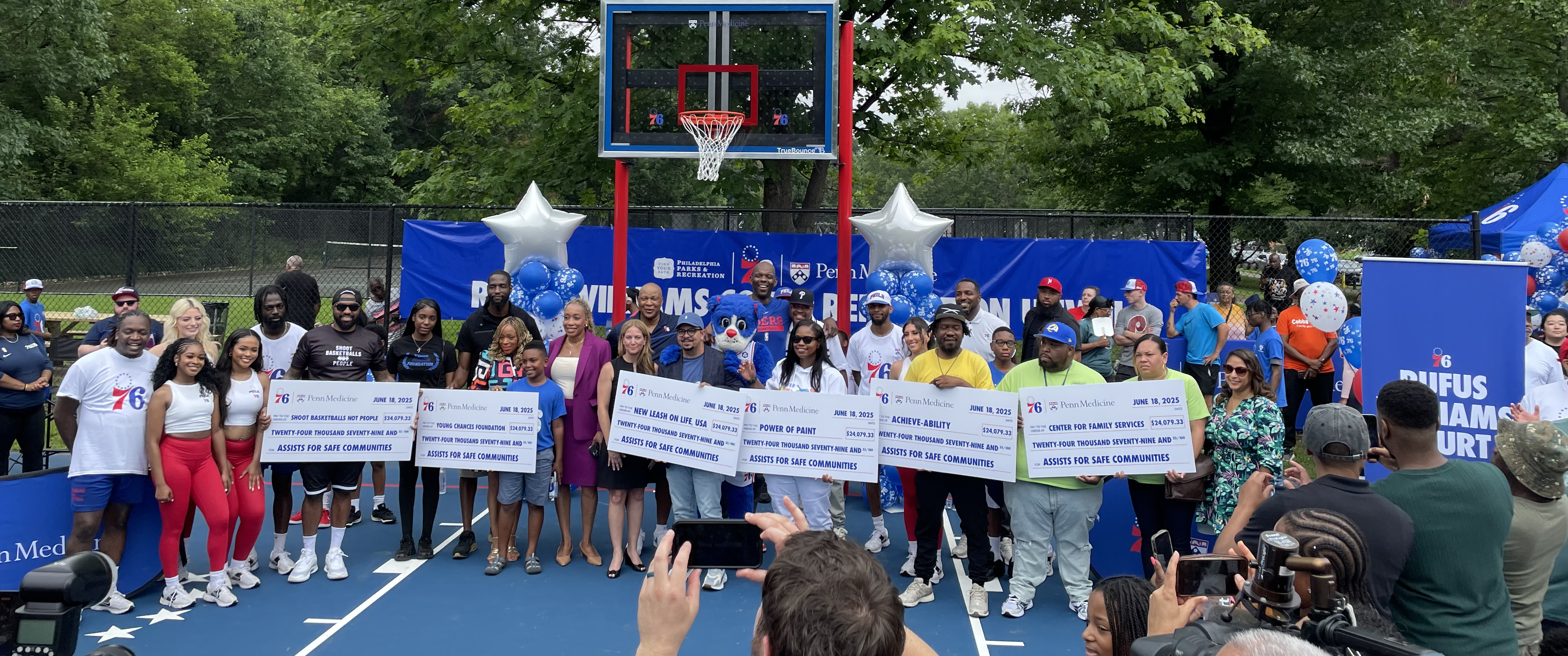 A group of people holding several large checks on a basketball court