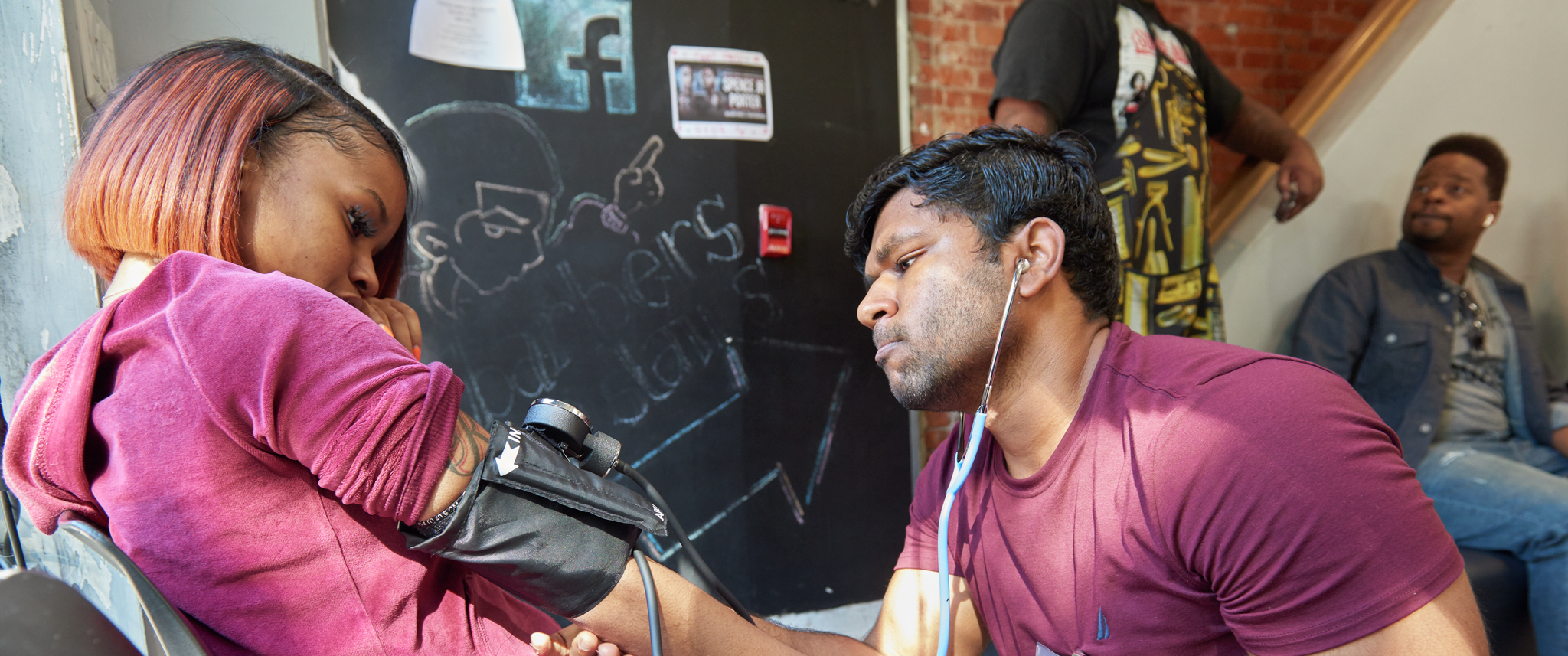 A medical student taking blood pressure of a barbershop patron