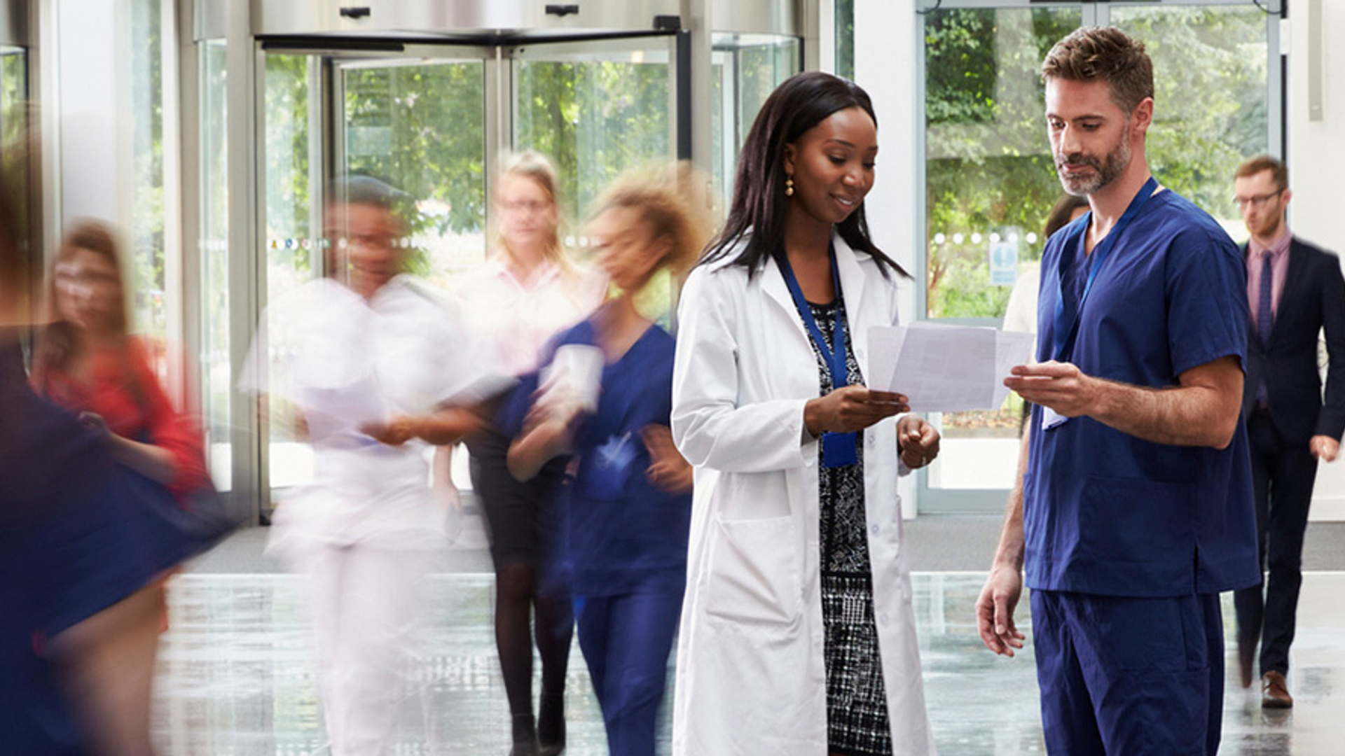 Health care professionals reviewing papers in hallway as others walk by