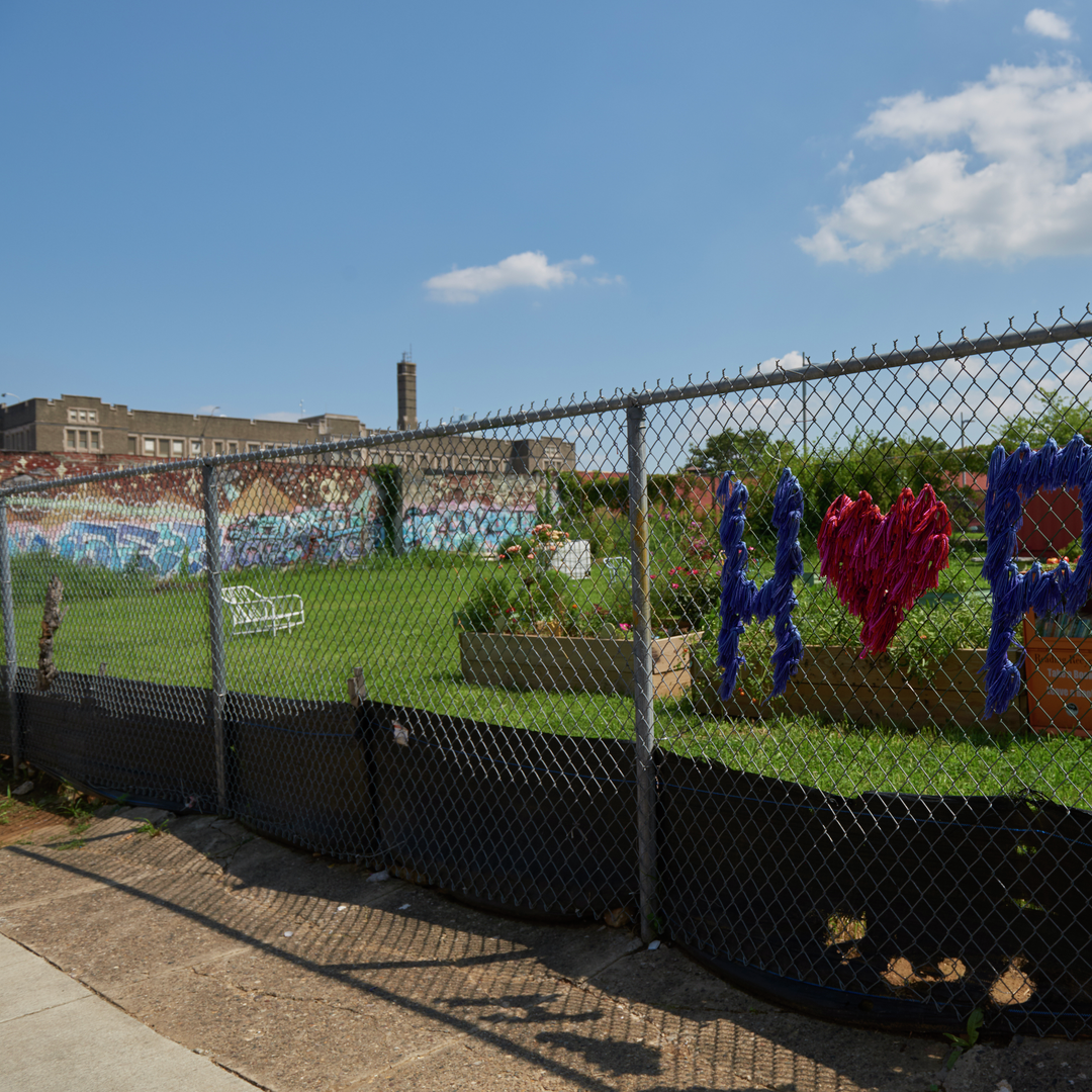 The word "hope" with a heart for the O is woven into a chain link fence separating a sidewalk from lawn