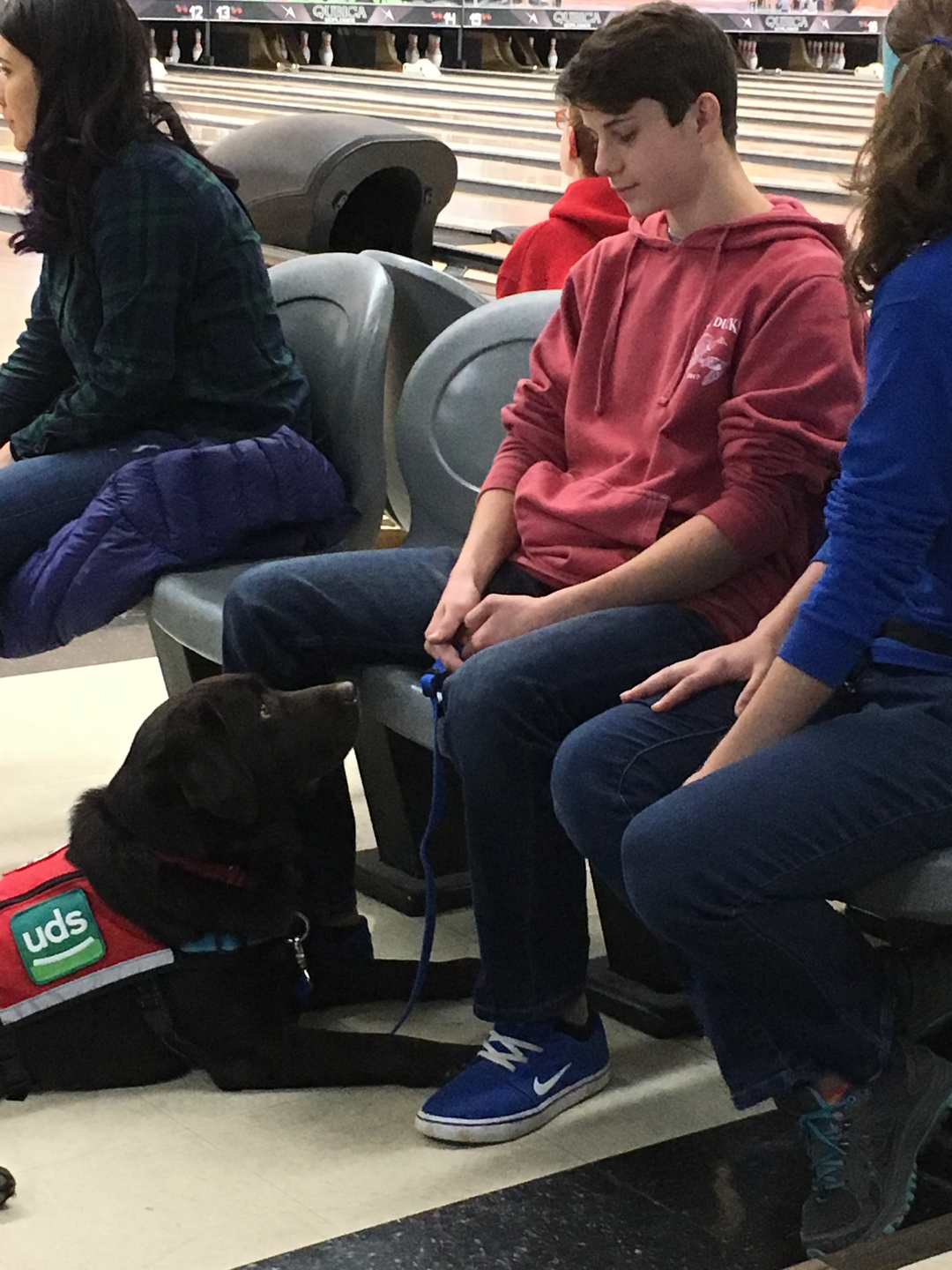 Maria Wright's teenage son sitting at a bowling alley with an UDS service dog.