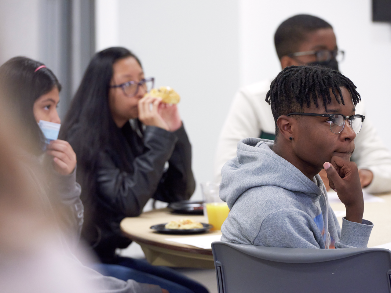 Teenage students of varied races sit in a classroom listening 